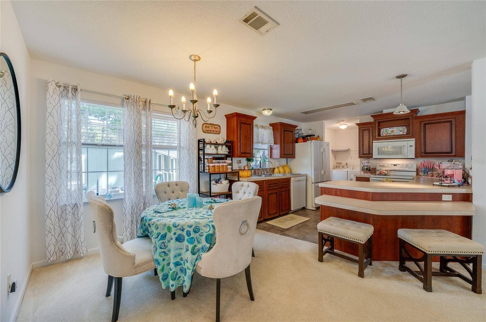 60 GOLDEN GATE CIRCLE, Port Orange, FL 32129 Dedicated dining area set alongside large windows with elegant hanging lighting fixtures. The layout transitions smoothly into the open kitchen equipped with ample cabinetry and counter space.