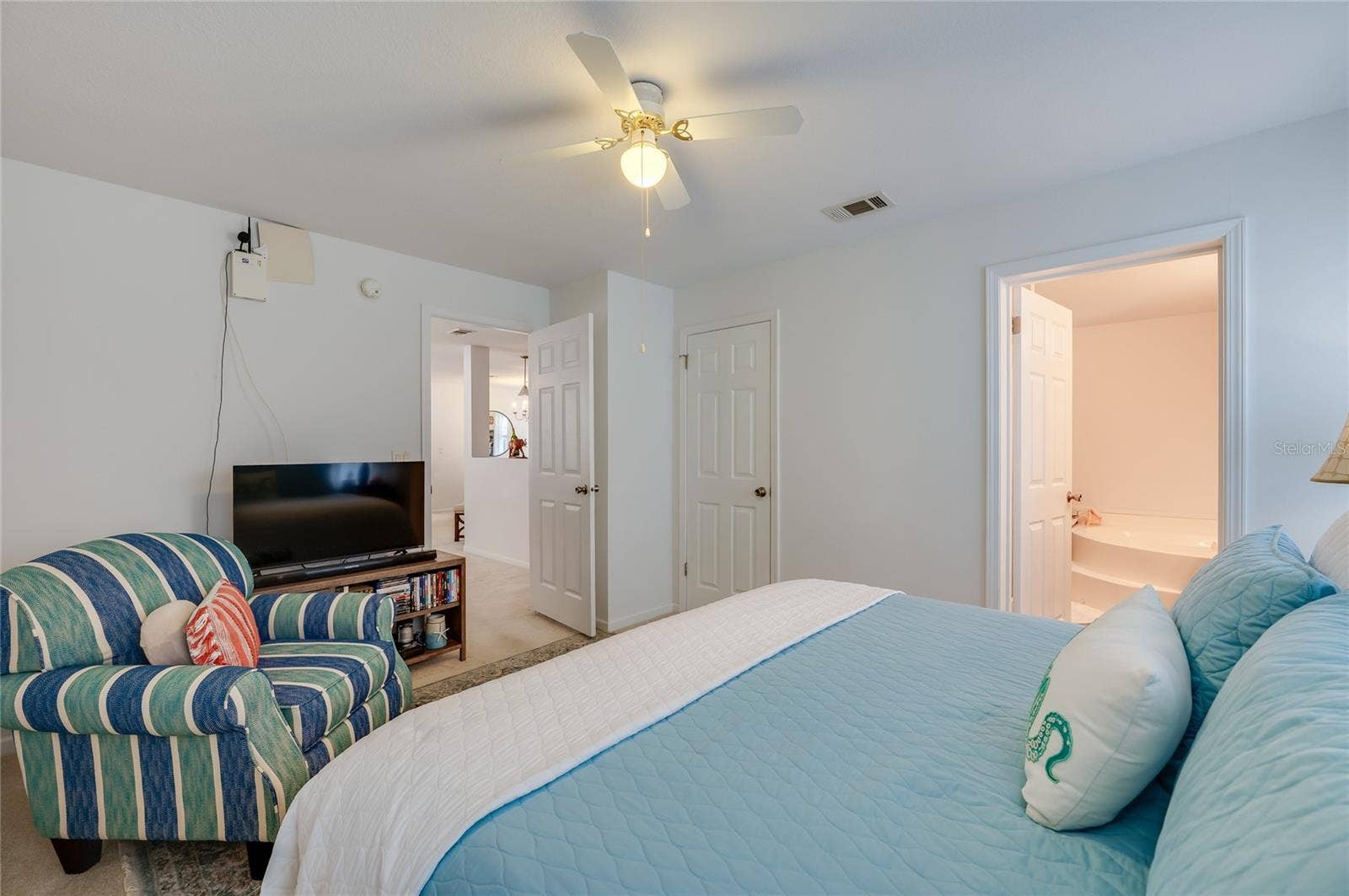 60 GOLDEN GATE CIRCLE, Port Orange, FL 32129 Spacious primary bedroom suite offering a built-in closet, ceiling fan, and open doorways leading to the home's main living area and private ensuite bathroom.