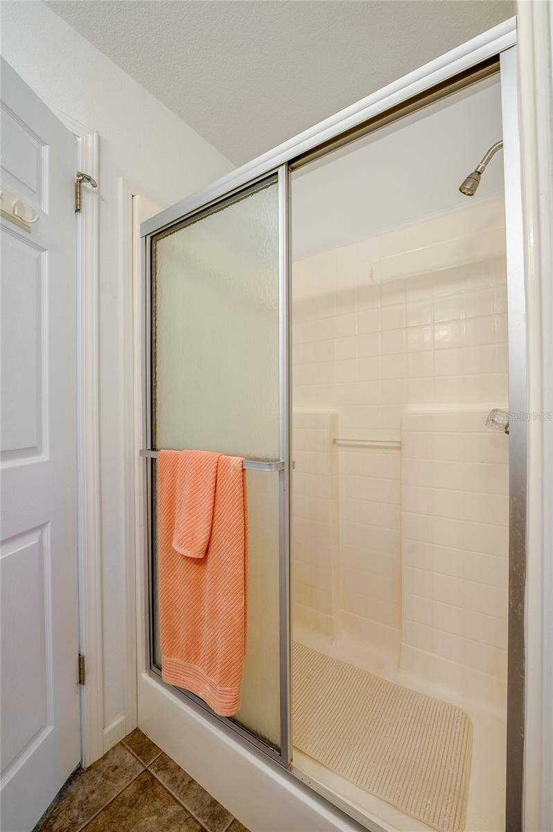 60 GOLDEN GATE CIRCLE, Port Orange, FL 32129 Walk-in shower enclosure featuring tiled walls and a sliding glass door.