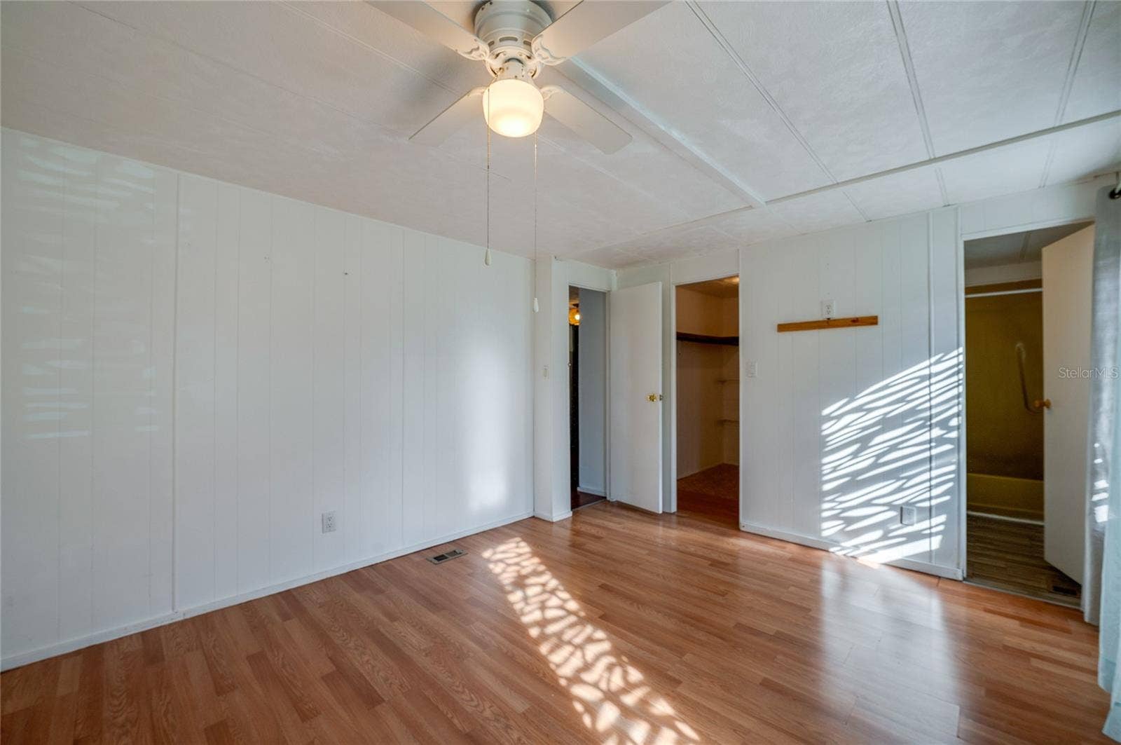 Additional view highlights the rooms open floor area, ceiling fan, and convenient access to a walk-in closet and adjoining bathroom.