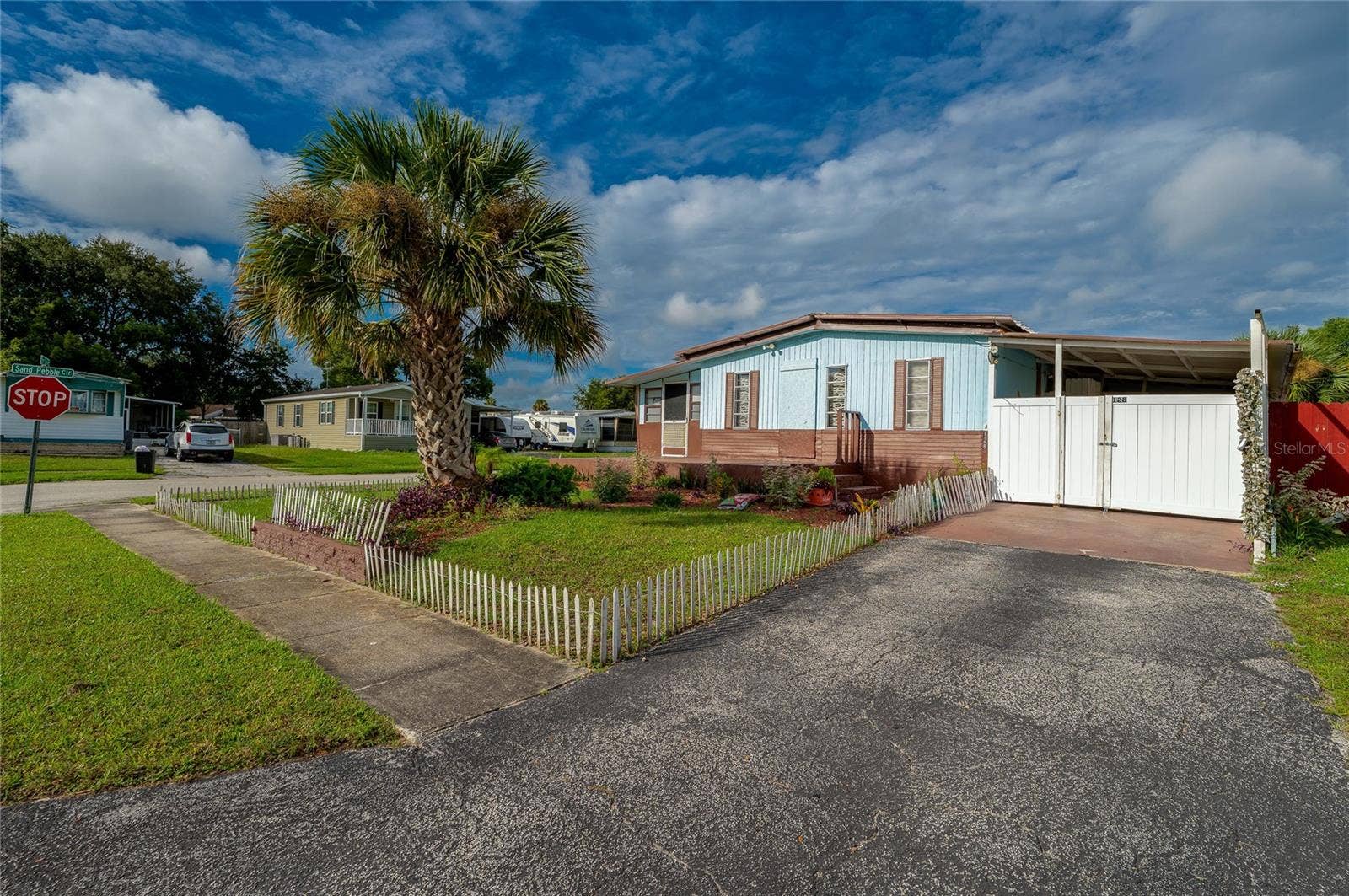 Front view showcases the homes landscaped yard, mature palm tree, driveway, covered parking area, and welcoming entry.