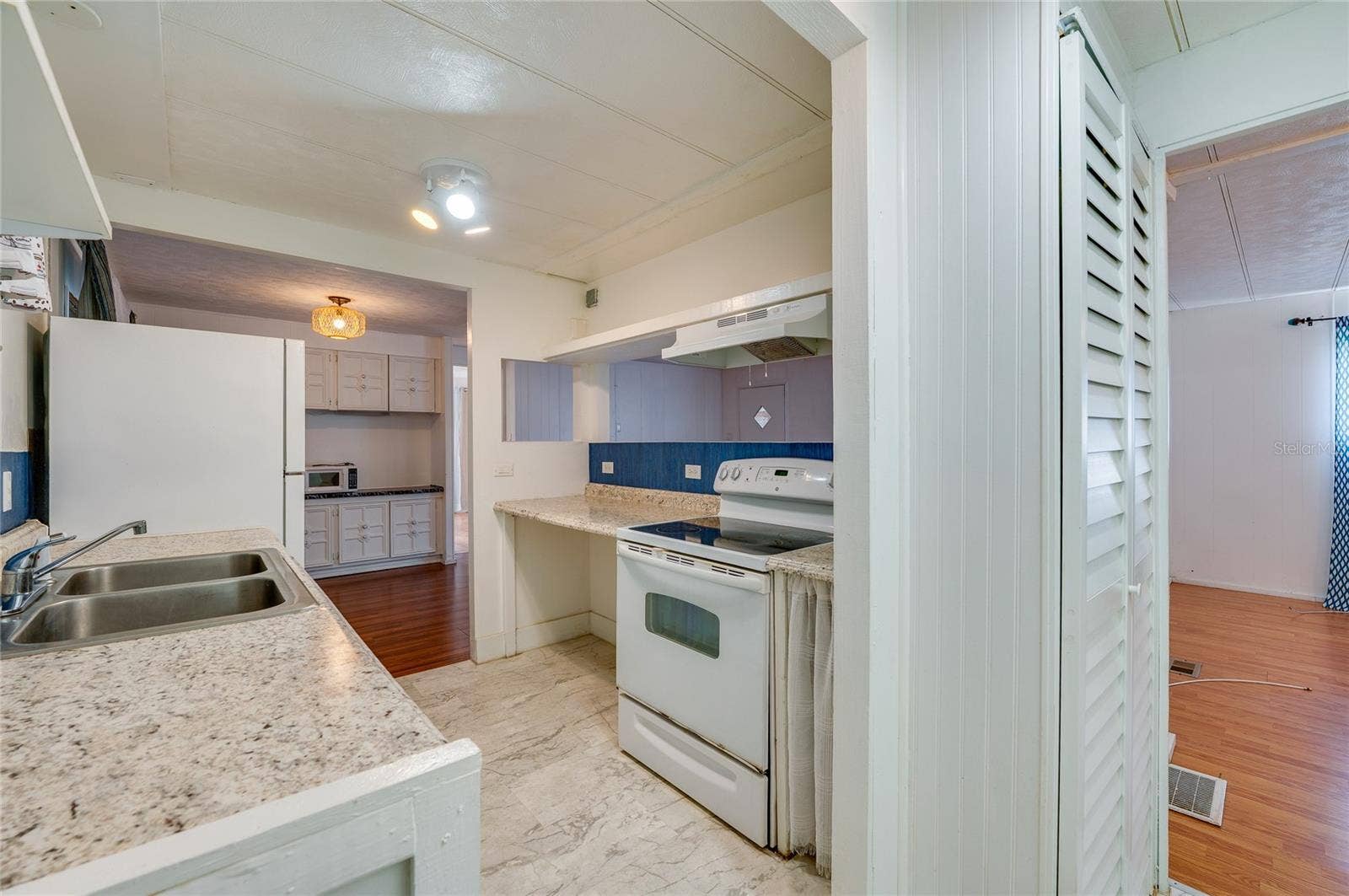 Functional eat-in kitchen features generous counter space, a double-basin sink, range with hood, refrigerator, and a pass-through opening that connects with the adjoining living area.