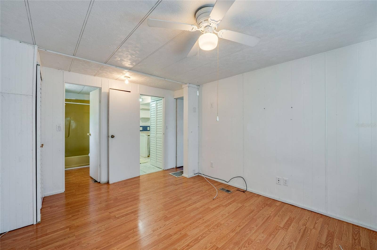 Another view highlights the rooms generous open floor area, ceiling fan, and convenient access to the adjoining bath and nearby living spaces.