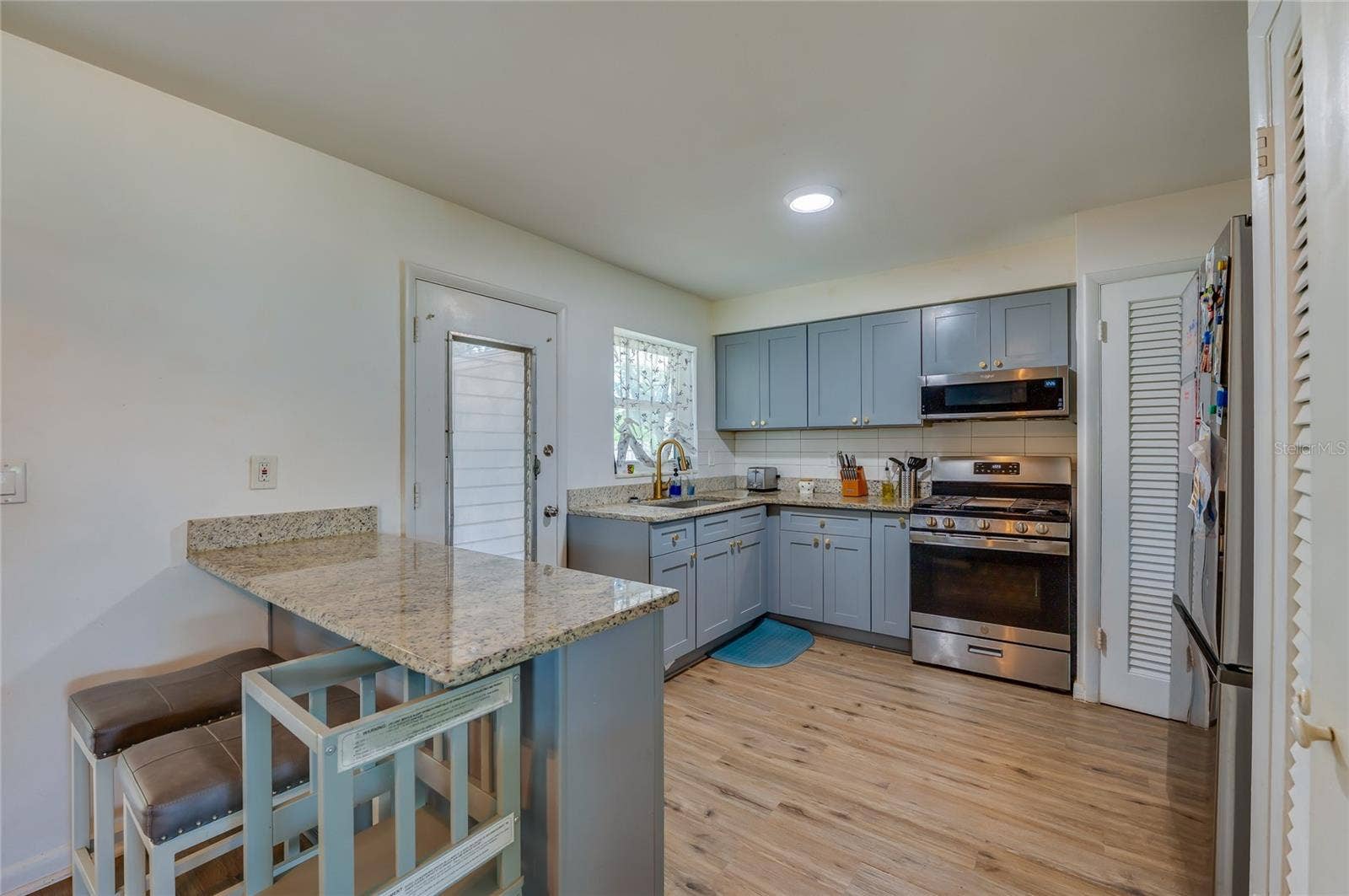 605 E NORMANDY BOULEVARD, Deltona, FL 32725 Functional kitchen layout displaying blue cabinetry, granite counter space, stainless steel appliances, and built-in breakfast bar overhangs.