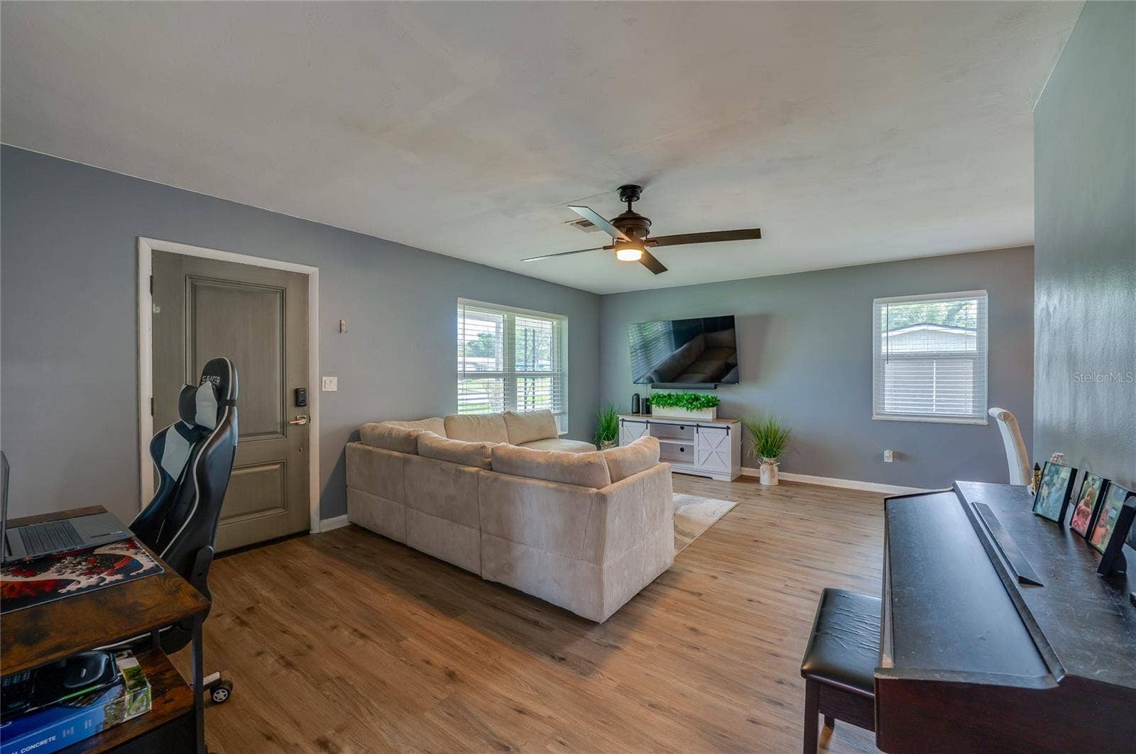 605 E NORMANDY BOULEVARD, Deltona, FL 32725 Open living area showing LVP floors, cool gray walls, a ceiling fan, and large windows that fill the space with light.