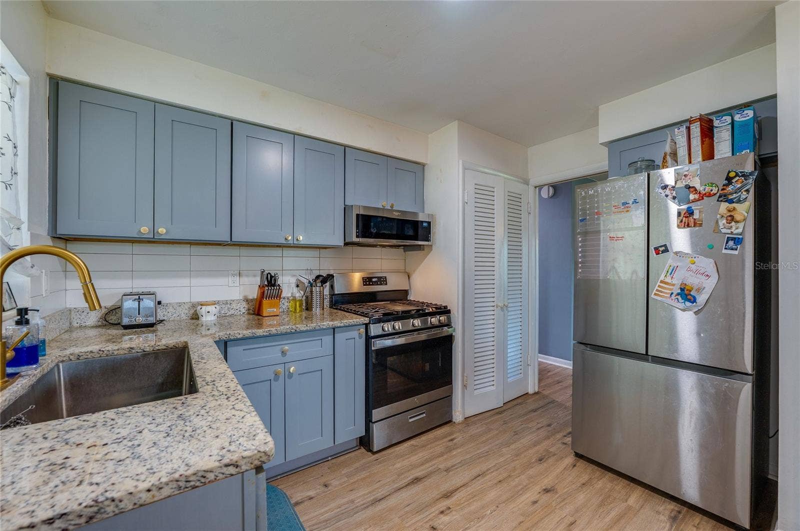 605 E NORMANDY BOULEVARD, Deltona, FL 32725 Modernized kitchen with stylish gray-blue cabinets, granite countertops, tile backsplash, and a large stainless steel refrigerator.