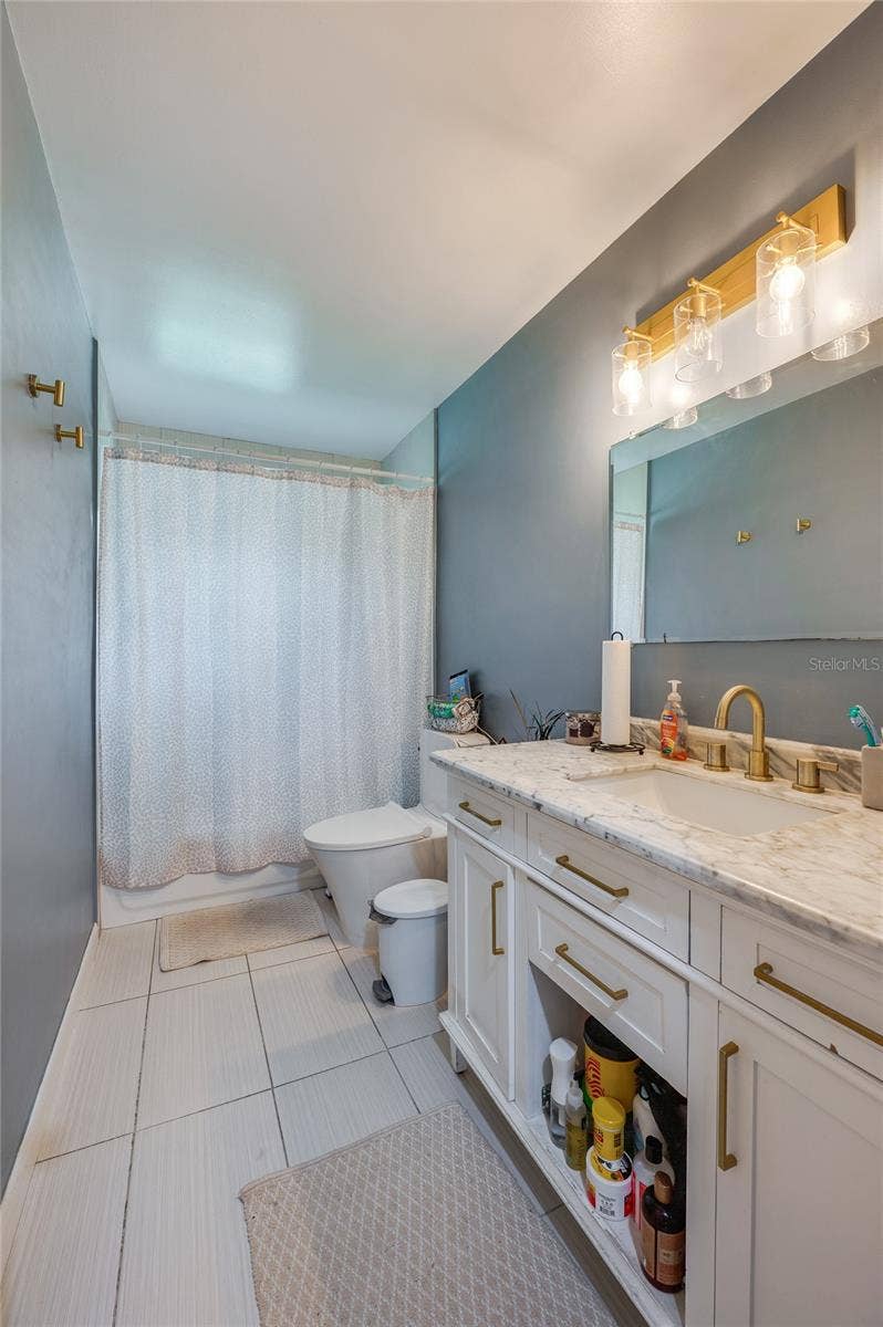 605 E NORMANDY BOULEVARD, Deltona, FL 32725 Bathroom displaying a single vanity with gold hardware, modern lighting fixtures, neutral tile flooring, and clean wall finishes.