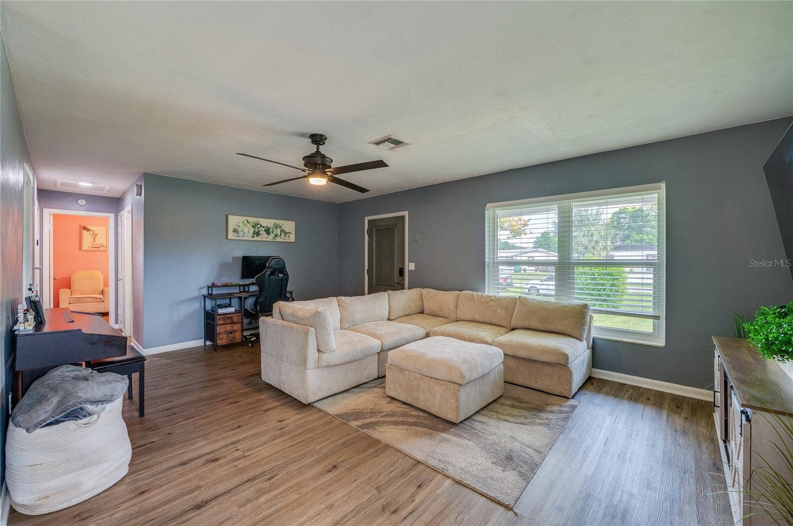 605 E NORMANDY BOULEVARD, Deltona, FL 32725 Generously sized main room featuring LVP flooring, soft gray walls, a central ceiling fan, and large front-facing windows.