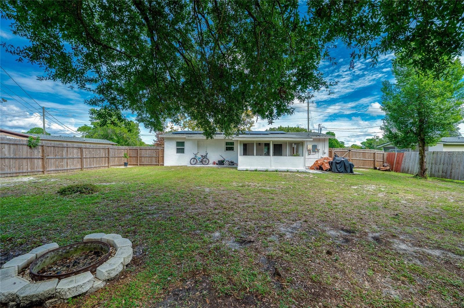 605 E NORMANDY BOULEVARD, Deltona, FL 32725 Generous rear lawn featuring a stone fire pit ring, full wood fencing, and direct views of the home's screened patio extension.