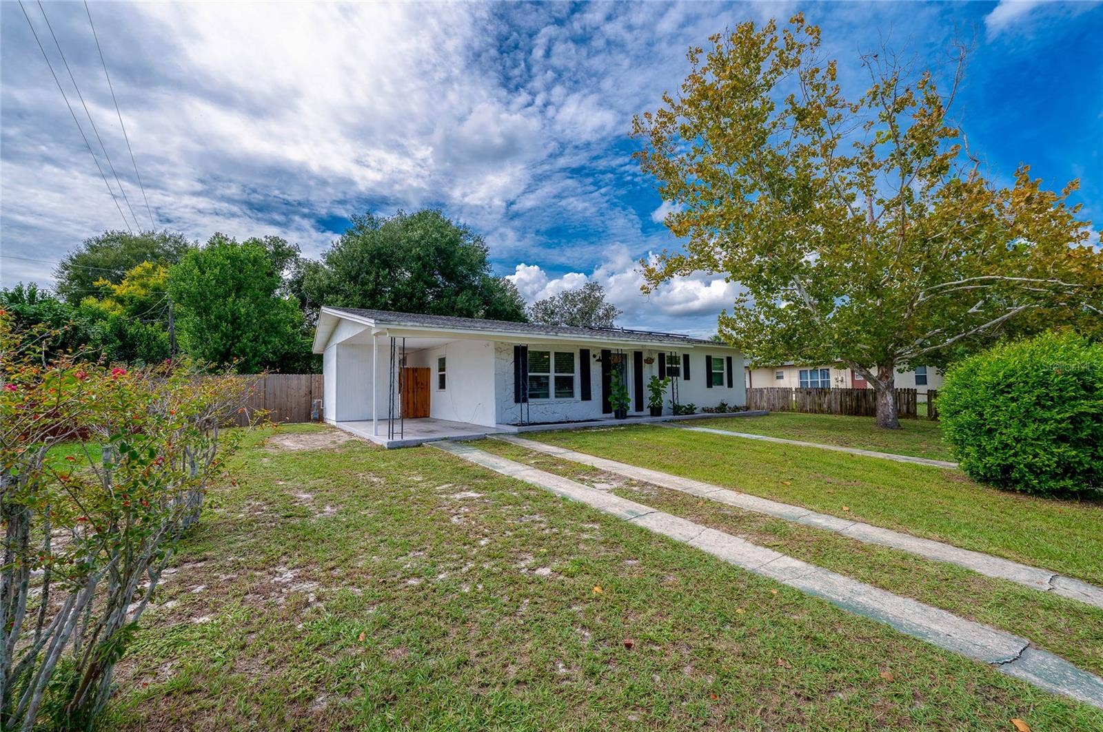 605 E NORMANDY BOULEVARD, Deltona, FL 32725 Exterior view highlighting the long concrete ribbon driveway, expansive front lawn, mature shade trees, and low-maintenance single-story design.