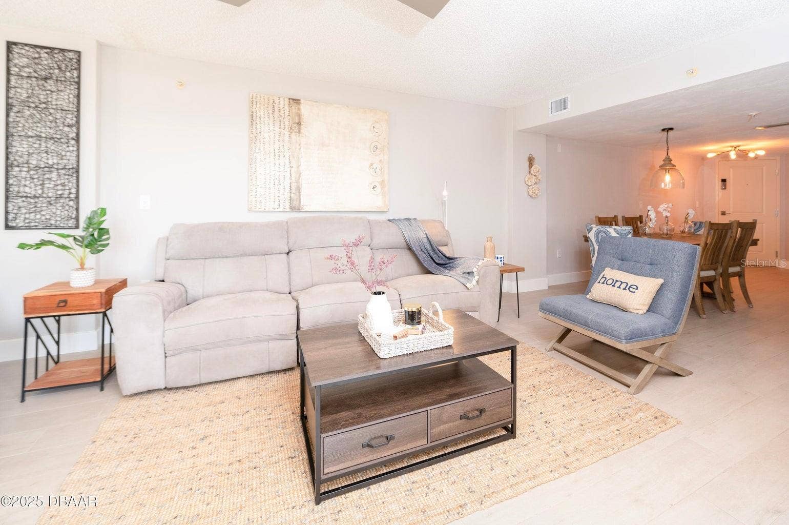 This inviting living room offers a comfortable gathering space with neutral finishes and an open connection to the dining area, ideal for relaxing after a day at the beach.