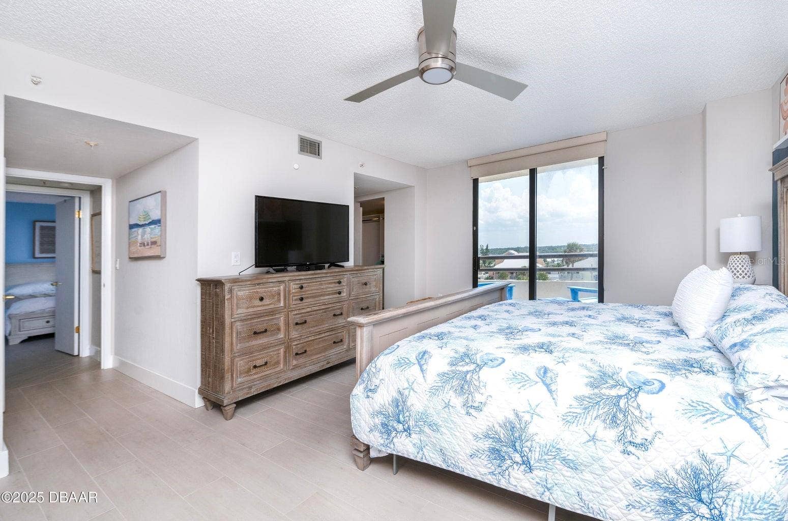 Another view of the generously sized primary bedroom showcases abundant natural light, neutral finishes, and direct balcony access, creating a comfortable coastal retreat.