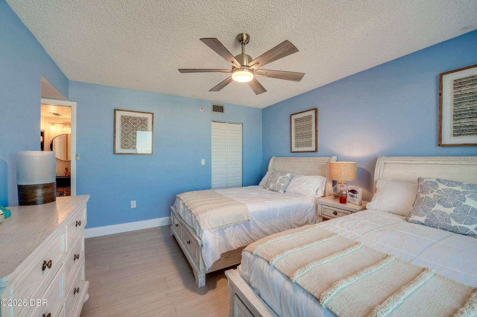 This inviting guest bedroom features soft blue walls, a contemporary ceiling fan, and coastal-inspired finishes, creating a bright and comfortable space for guests.