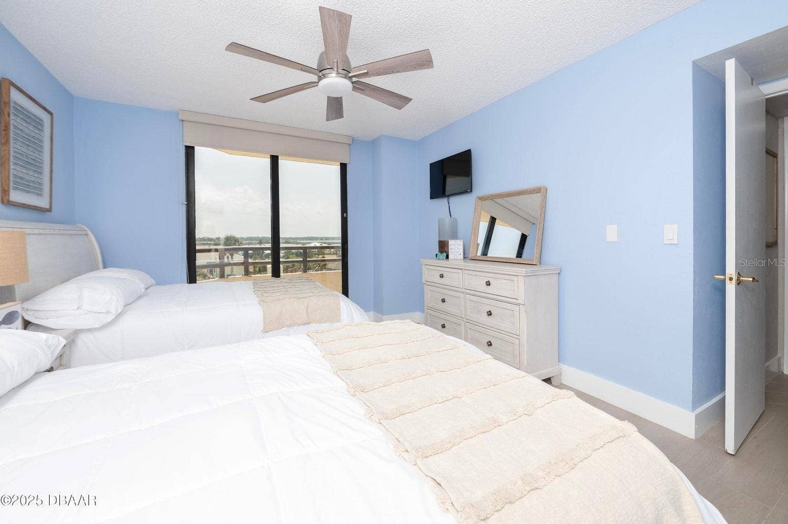 The guest bedroom offers sliding glass doors opening to a private balcony with inland views, allowing natural light to fill the room while extending the living space outdoors.