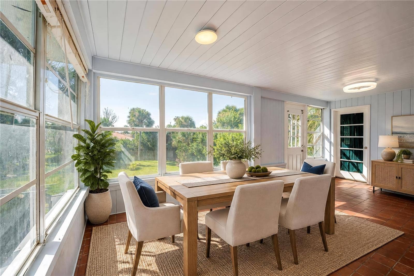 Virtually Staged - Breakfast nook featuring red tile floors, light-colored wood paneling, flush-mount ceiling lights, and wide windows overlooking the green backyard. Exterior glass doors provide easy access to the lawn and surrounding grounds.