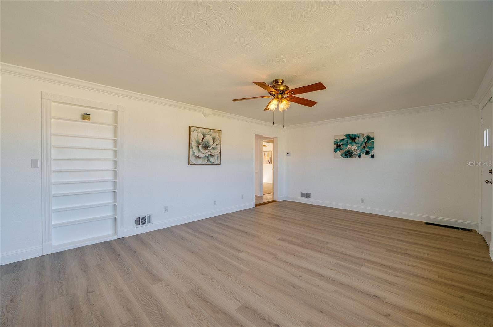 Open-concept living space framed by crisp white trim, continuous LVP flooring, and a built-in recessed wall shelving unit. The clean layout and central doorway provide an airy, connected atmosphere.