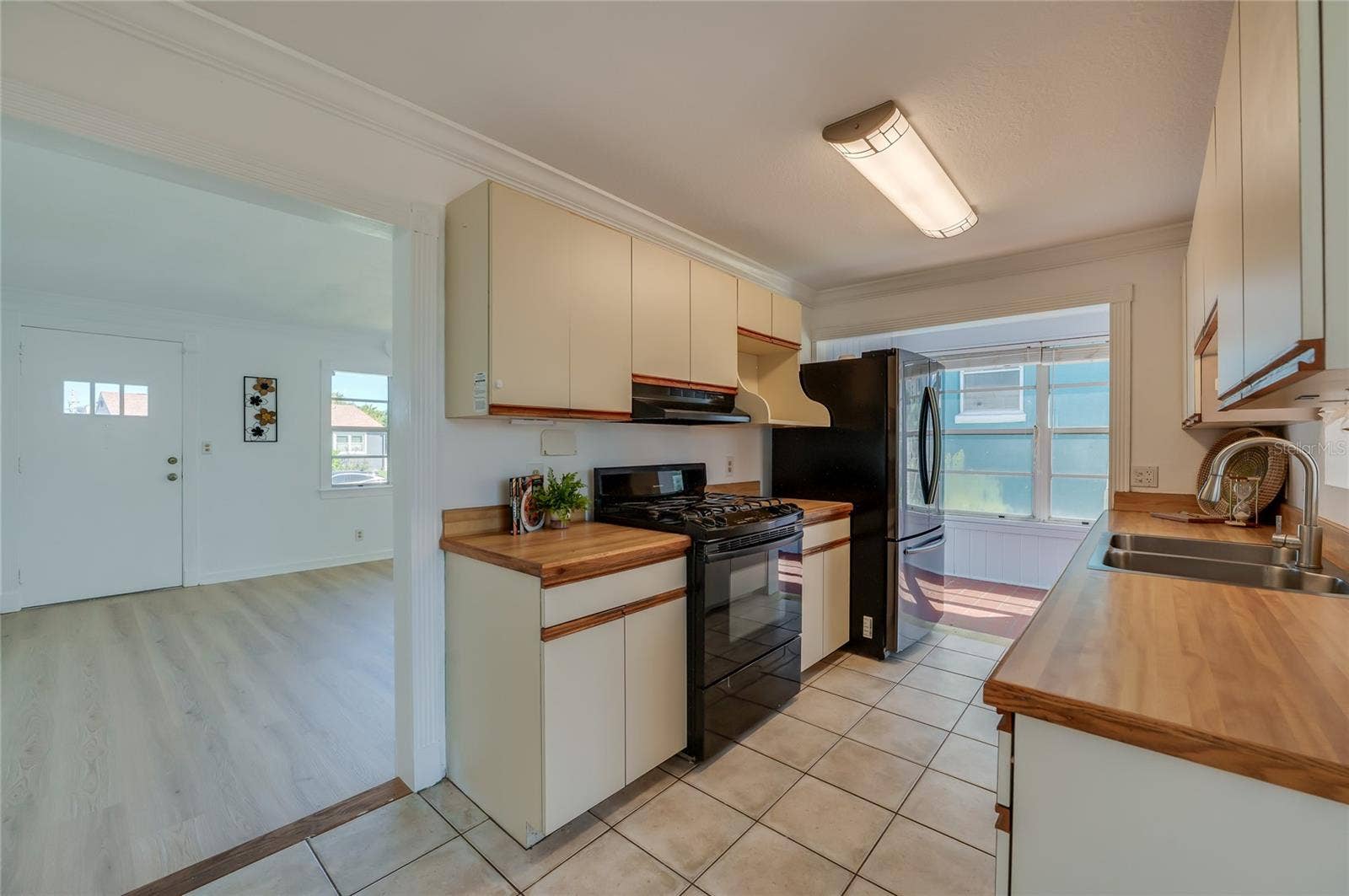 Efficient kitchen layout showcasing overhead cabinet storage, a gas range stove with range hood, and tile flooring. The open entryway offers a clear view into the adjoining bright living space.