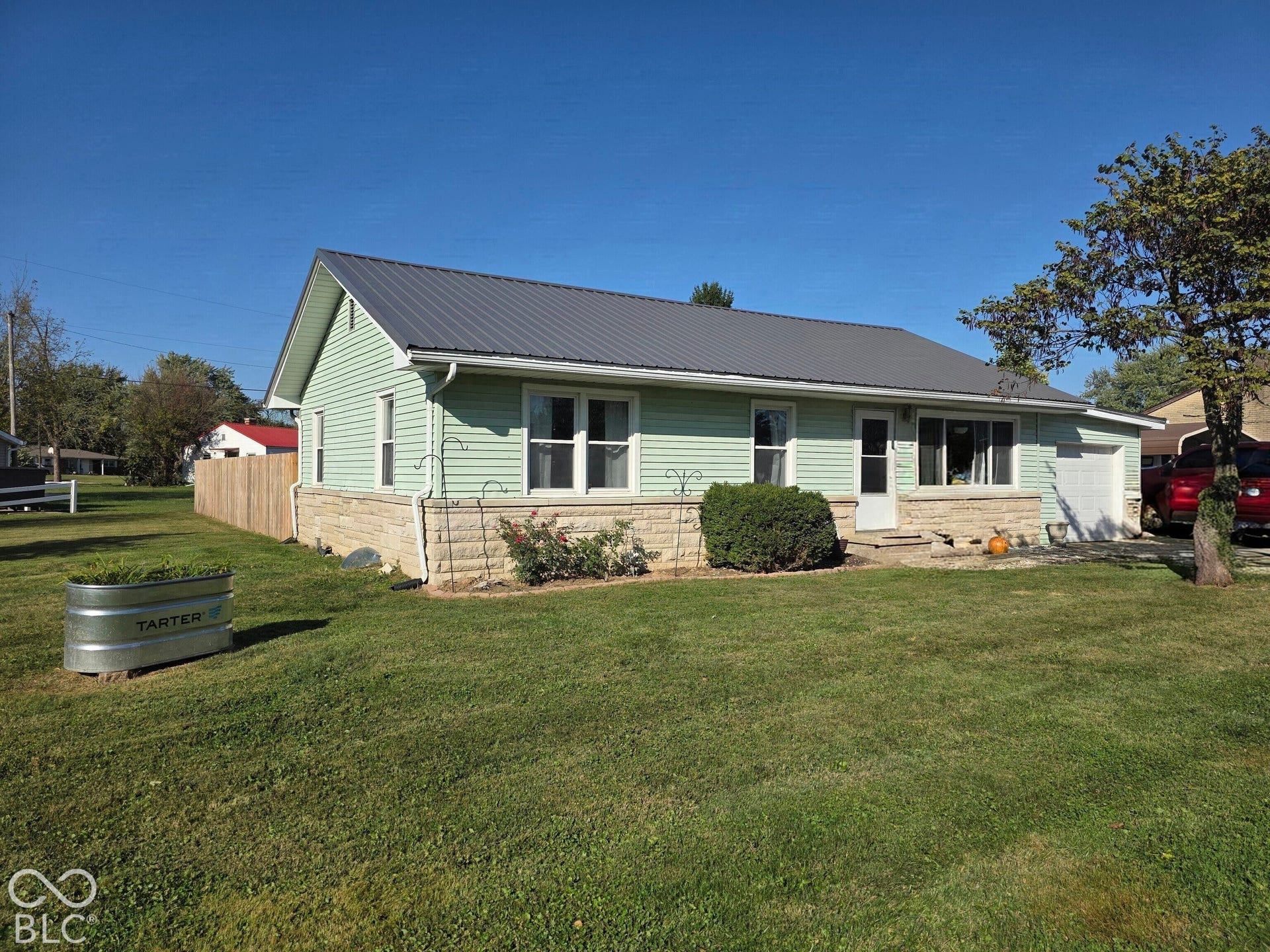Exterior featuring light green horizontal siding, stone veneer base, metal roofing, and an attached garage