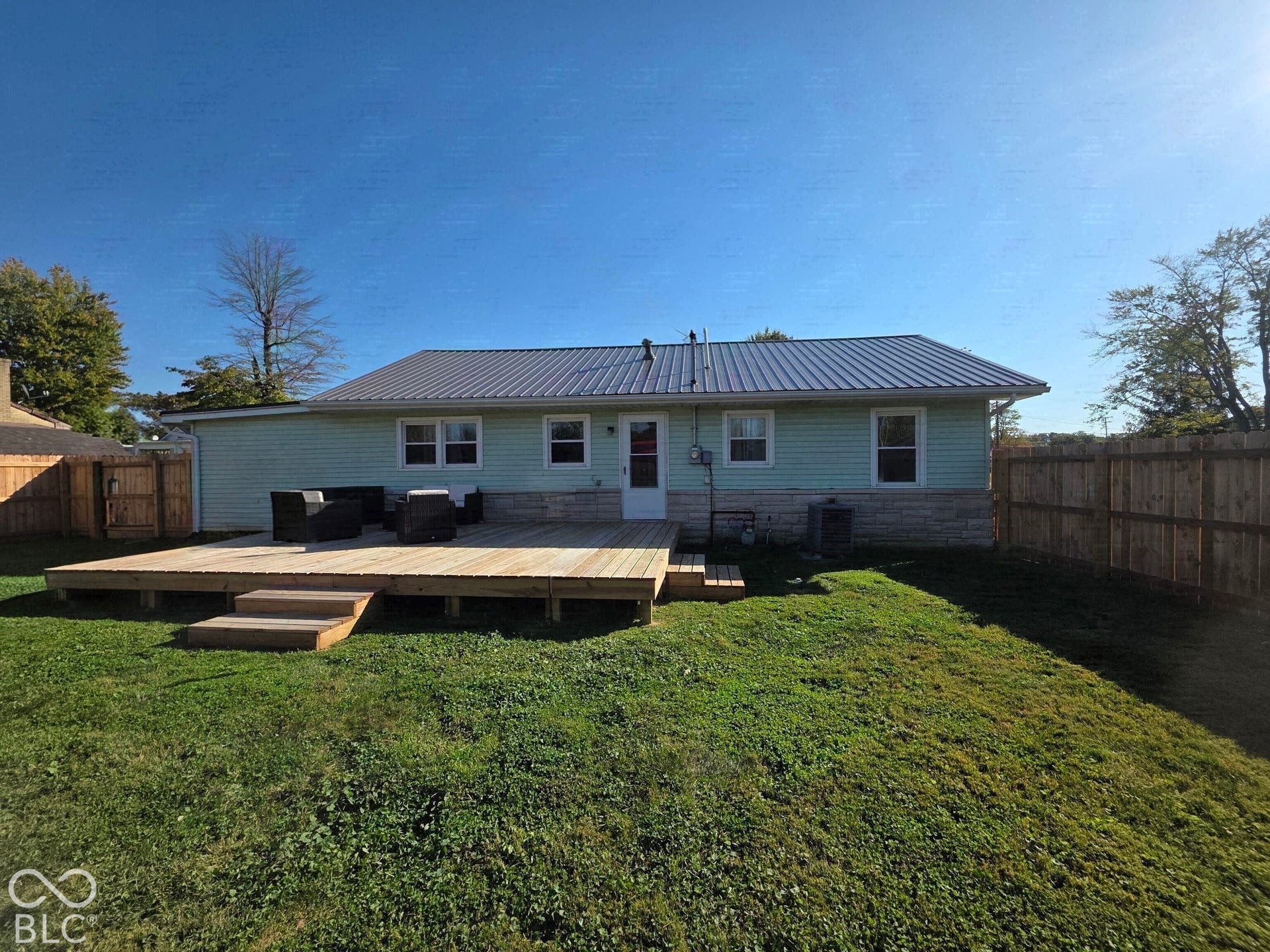 Rear exterior featuring a metal roof, stone veneer accents, wood decking, and privacy fencing