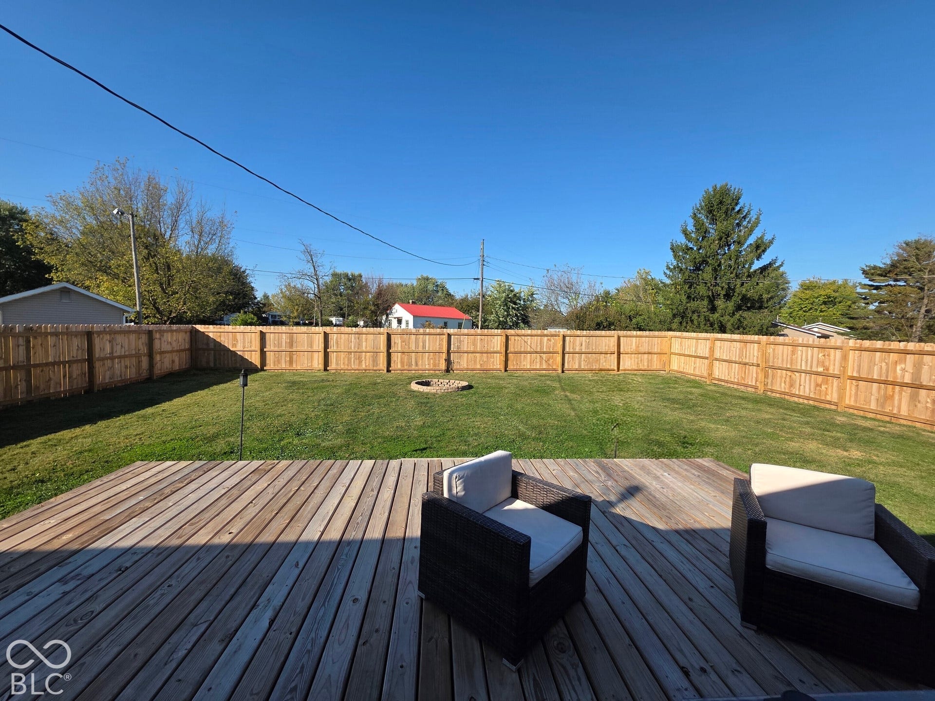 Backyard featuring a wood deck, manicured lawn, full-perimeter wood privacy fencing, and a stone-bordered fire pit
