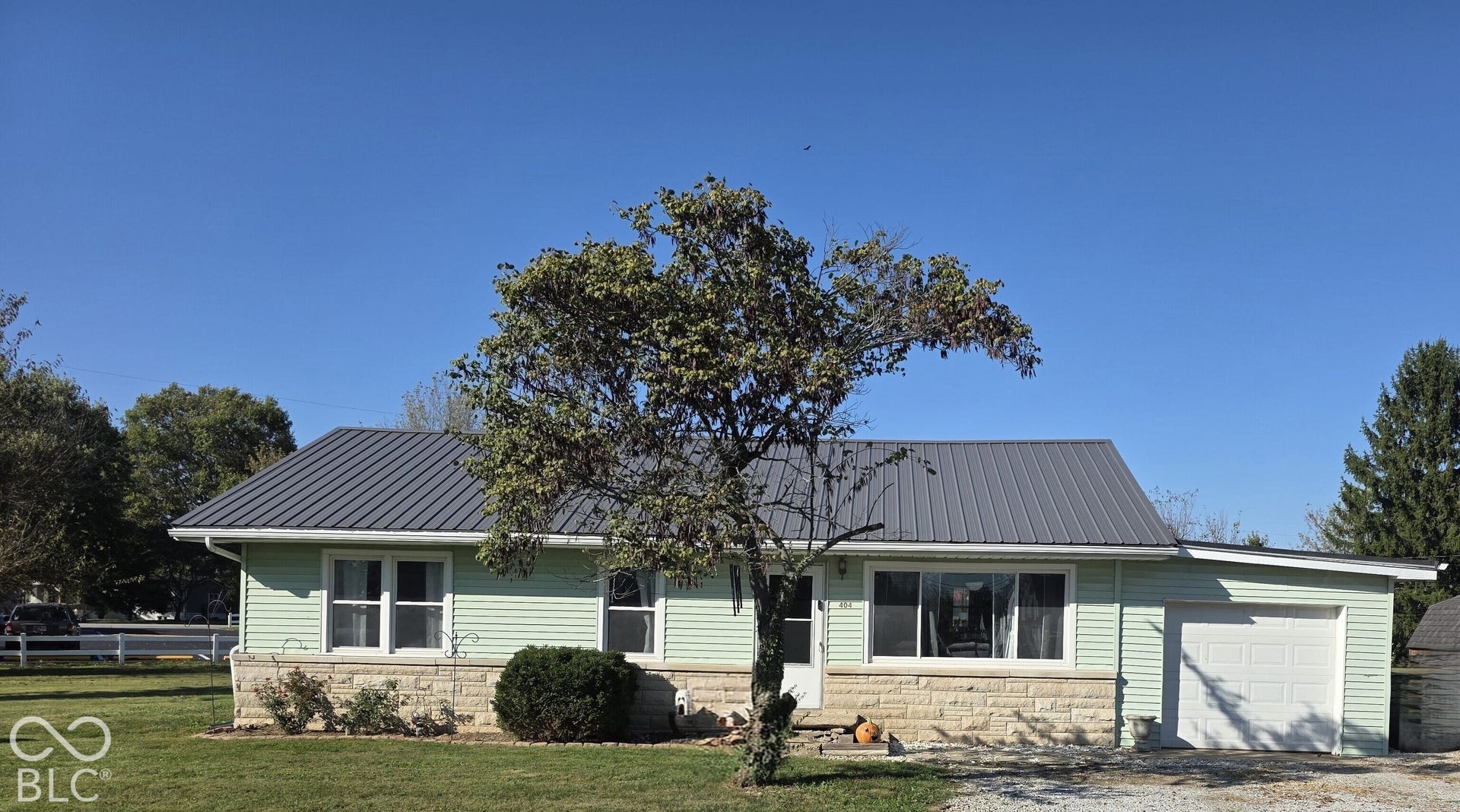 Single-story exterior featuring light-colored horizontal siding, a natural stone veneer base, a metal roof, and an attached one-car garage