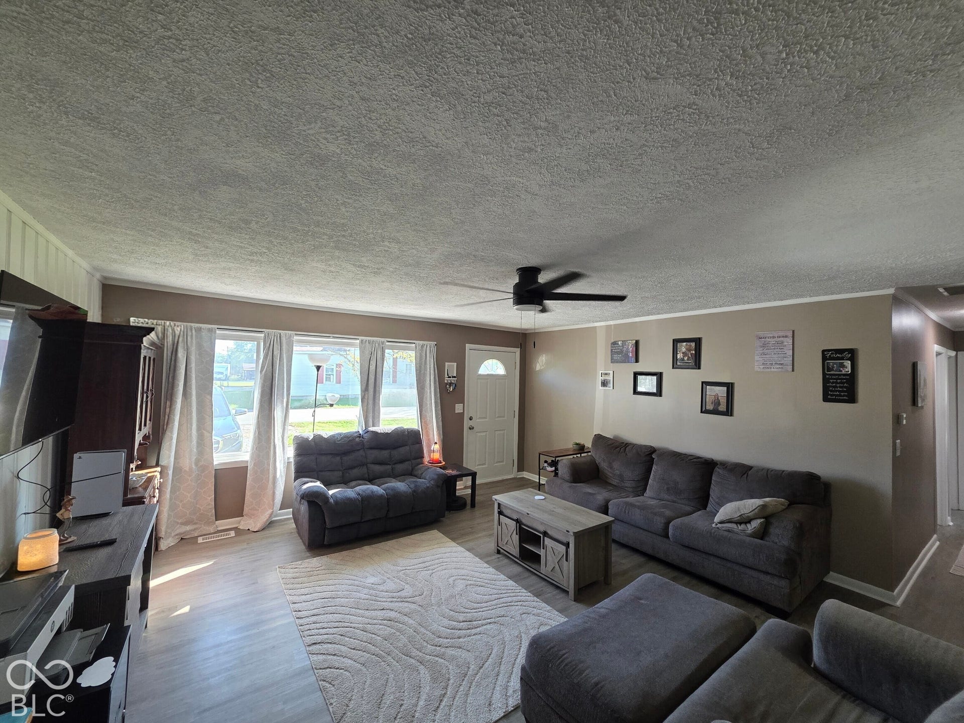 Living area featuring wood-finish flooring, ceiling fan, and large windows providing natural light