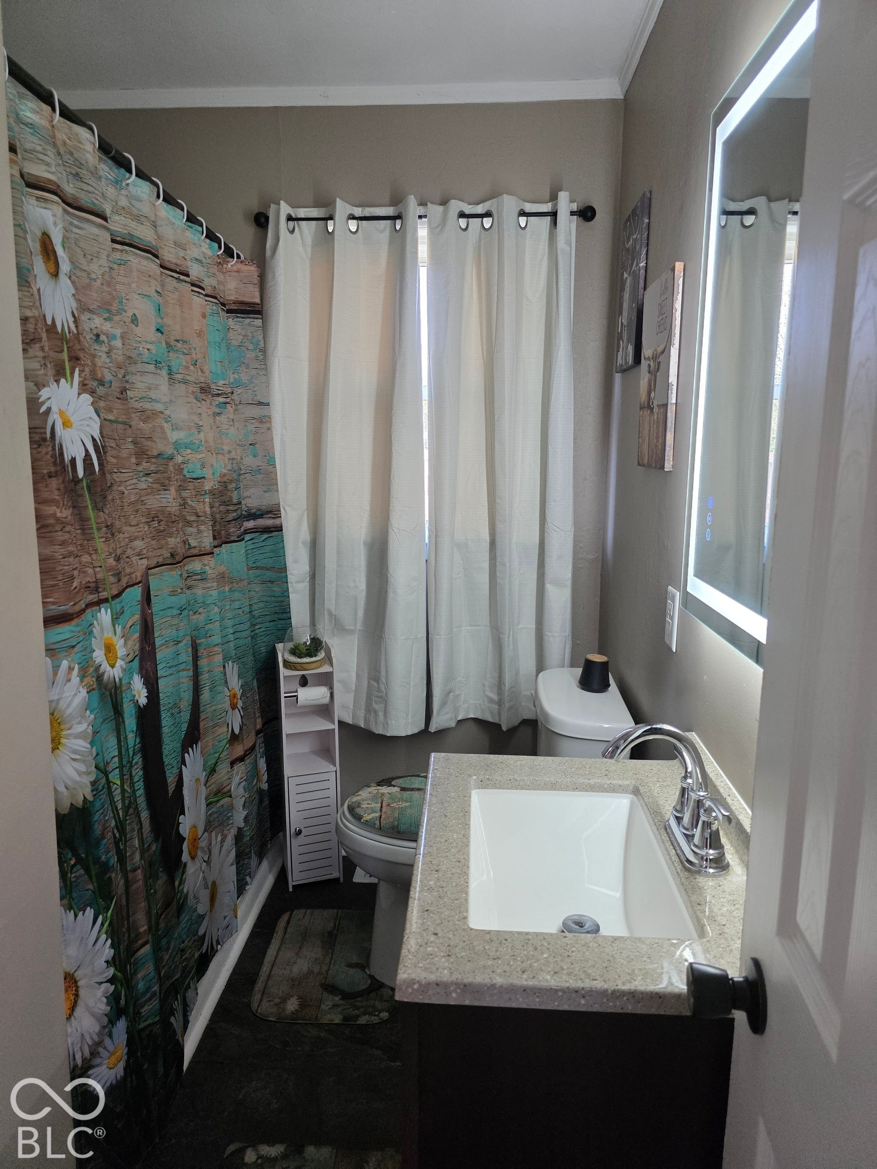 Bathroom featuring a vanity with a stone-composite countertop, integrated rectangular sink, chrome dual-handle faucet, and an integrated LED backlit wall mirror