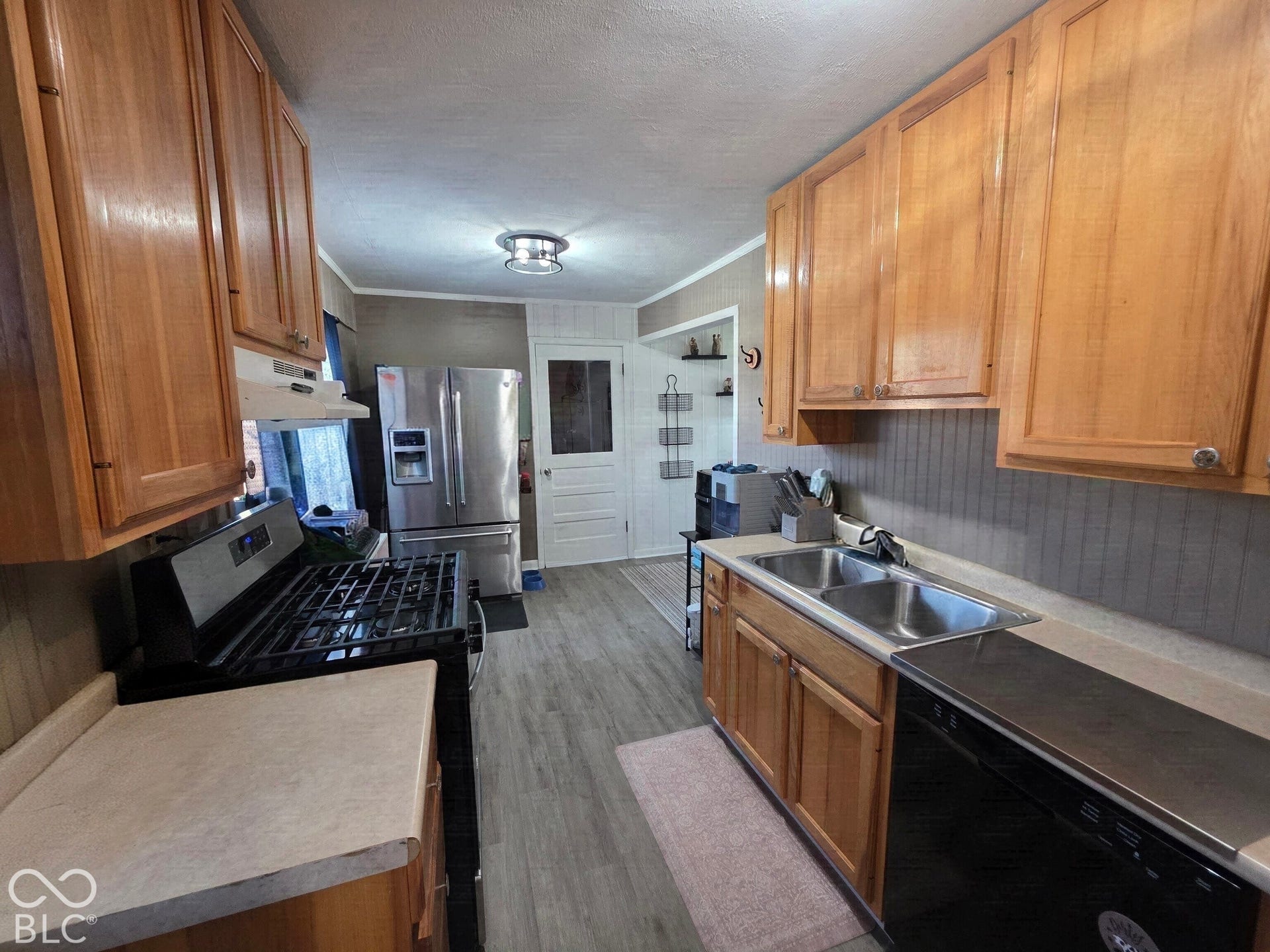 Kitchen featuring wood cabinetry, stainless steel refrigerator, dual-basin stainless steel sink, wood-finish flooring, and a gas range