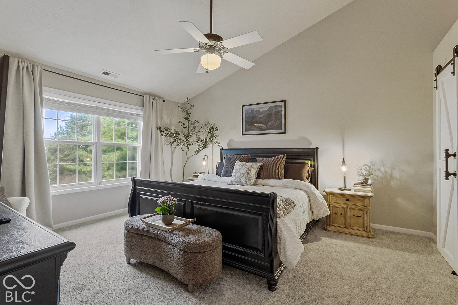 Retreat to this beautifully appointed primary bedroom, featuring abundant natural light, soft neutral finishes, and a spacious layout. A large window overlooks mature greenery, creating a peaceful connection to the outdoors and providing the perfect