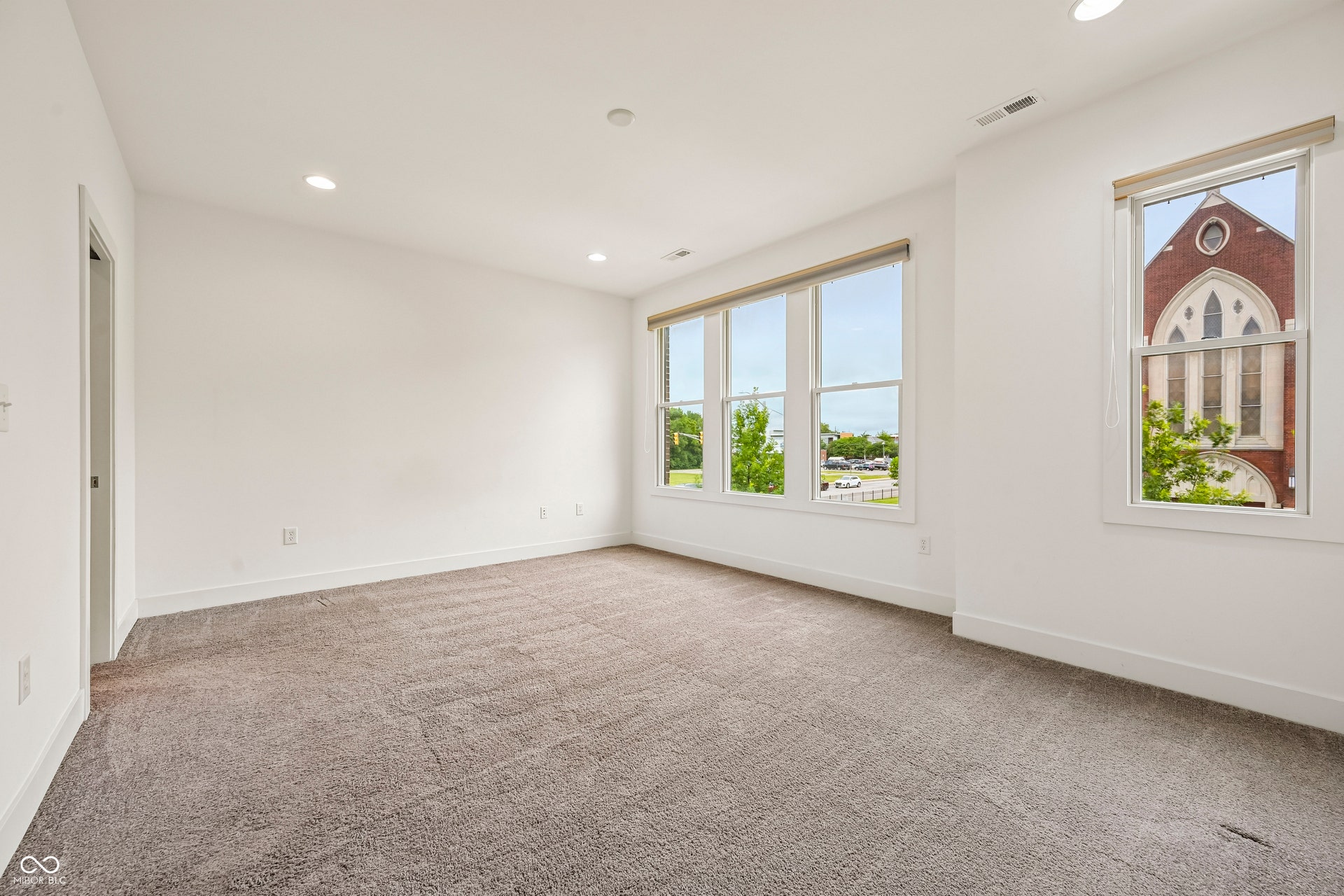 Spacious room featuring neutral carpeting, white walls, recessed lighting, and multiple windows