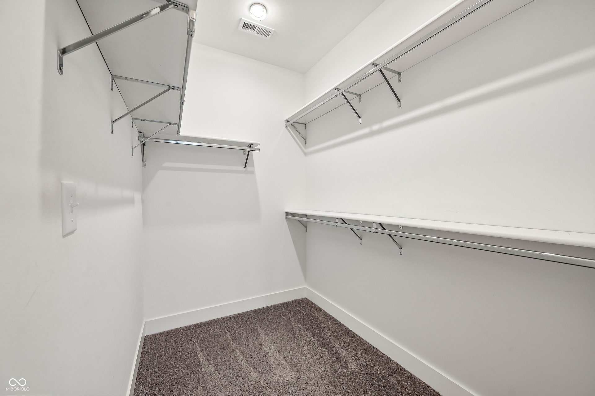 Walk-in closet featuring white walls, multi-level shelving, chrome hanging rods, recessed lighting, and textured carpet flooring