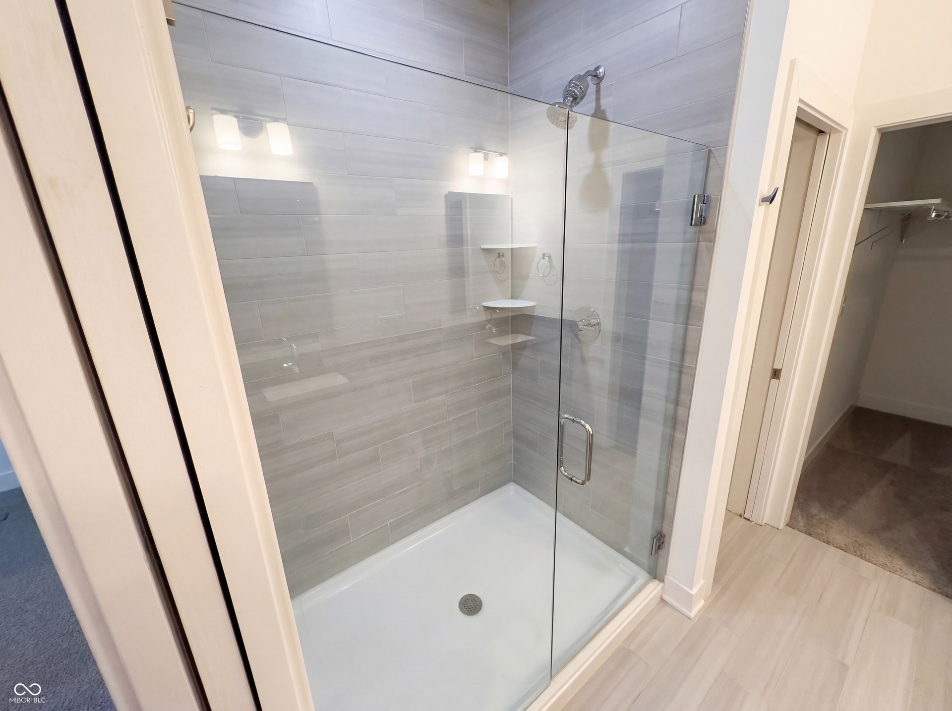 Spacious shower featuring a glass enclosure, light gray tile surround, and built-in shelving