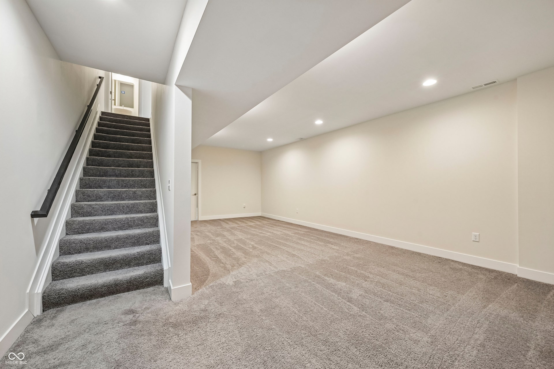 Finished basement featuring recessed lighting, a carpeted staircase with a dark handrail, a neutral color palette, and broadloom carpeting