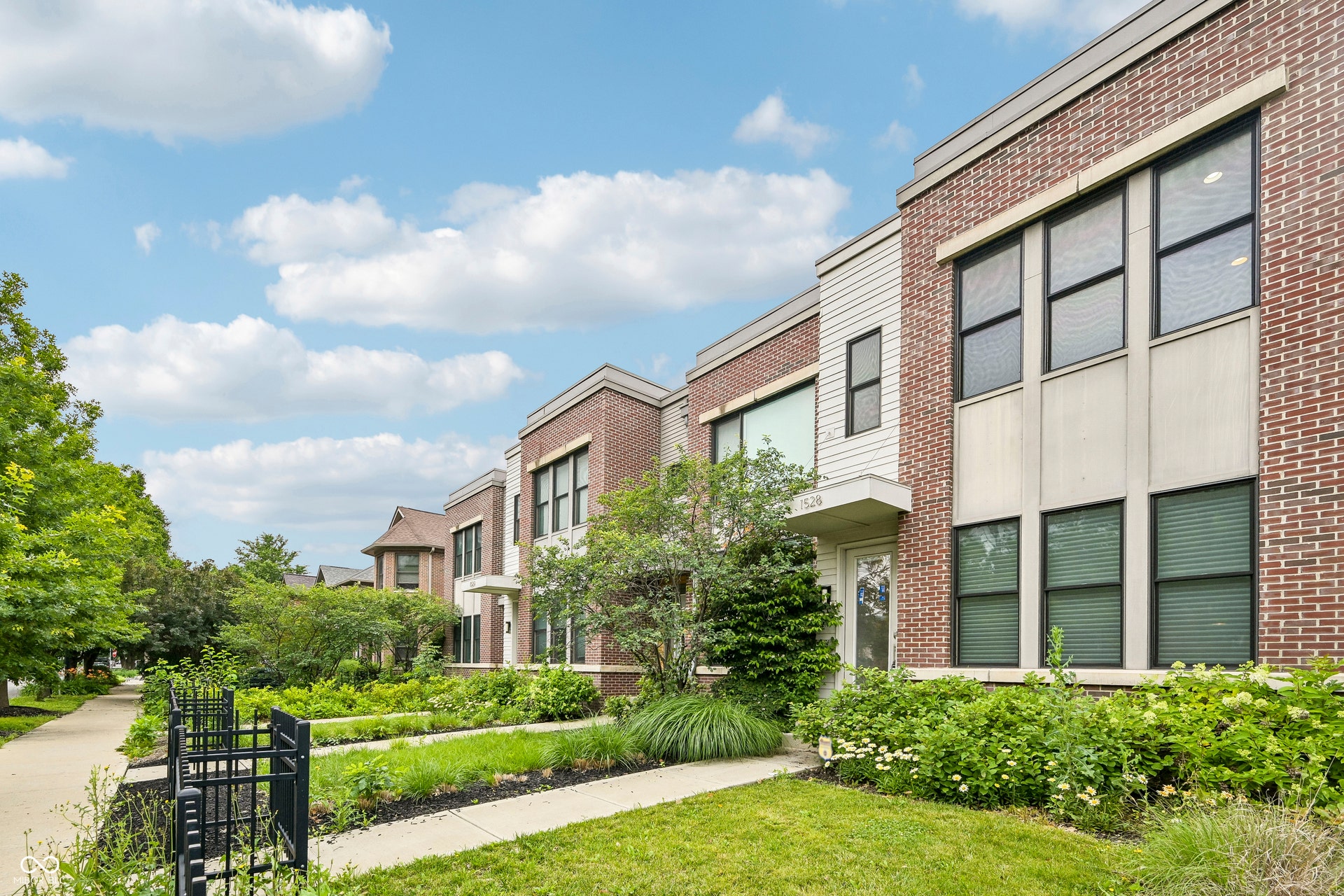 Modern townhome exterior featuring brick and horizontal siding, large windows with dark frames, and a glass-paneled entry door