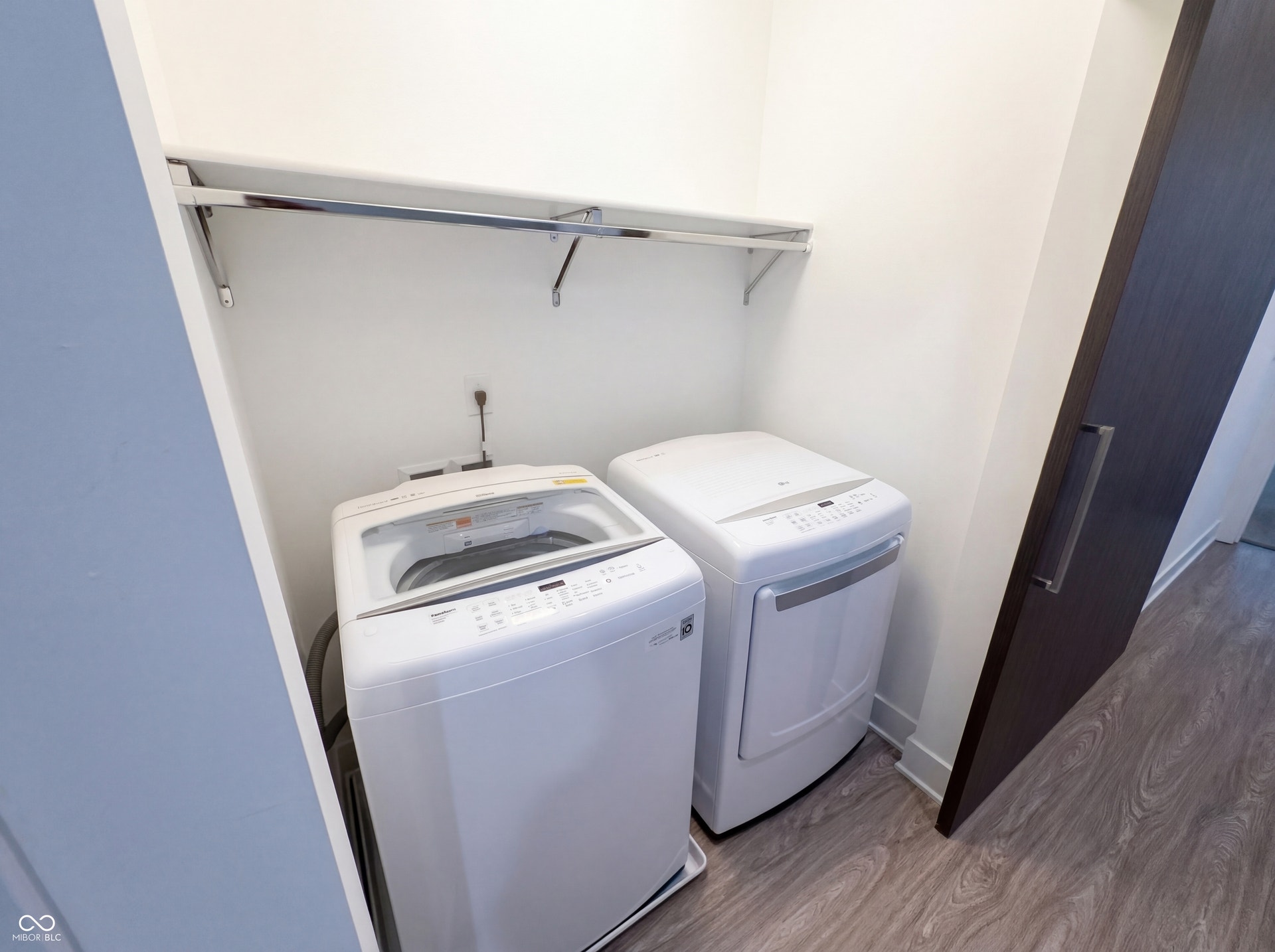 Dedicated laundry area featuring a top-load washing machine, front-load dryer, and overhead shelving with a hanging rod