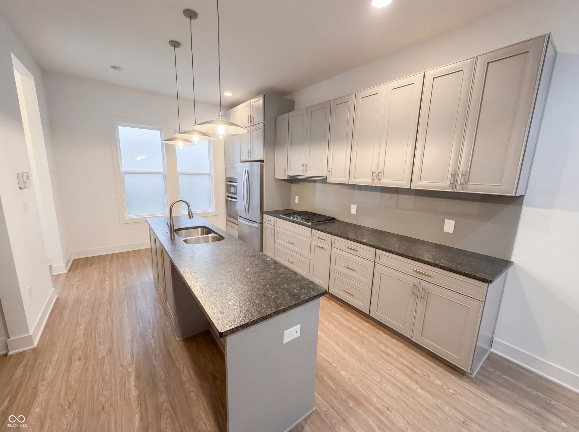 Kitchen featuring an island with an integrated sink and gooseneck faucet, light grey cabinetry with brushed nickel hardware, dark speckled countertops, stainless steel appliances, and wood-finish flooring