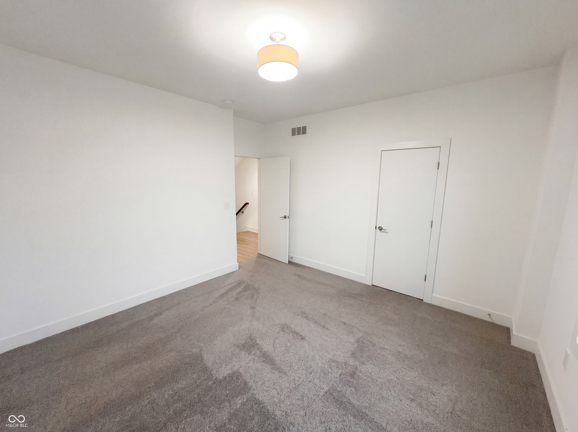 Spacious room featuring neutral carpeting, white walls, and a contemporary ceiling light fixture