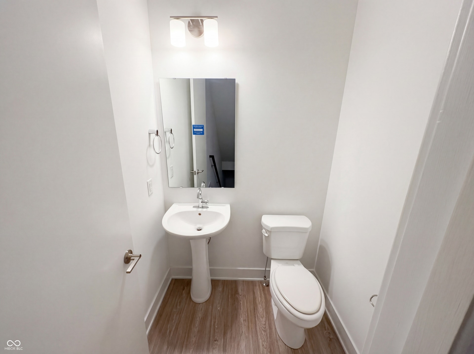 Powder room featuring a pedestal sink, white toilet, chrome fixtures, wood-finish flooring, and a contemporary vanity light