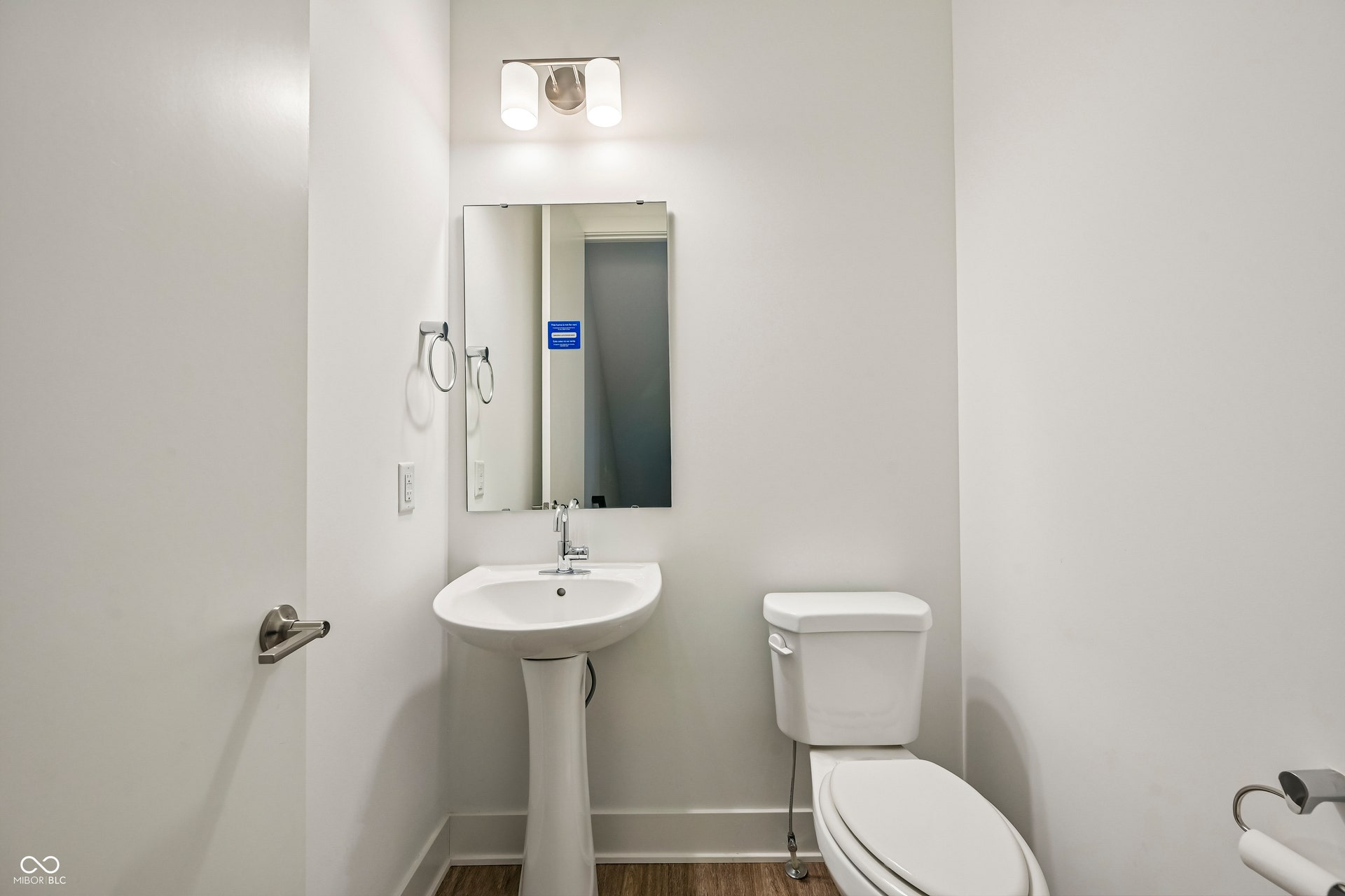 Pedestal sink with chrome faucet, vanity mirror, and overhead sconce lighting