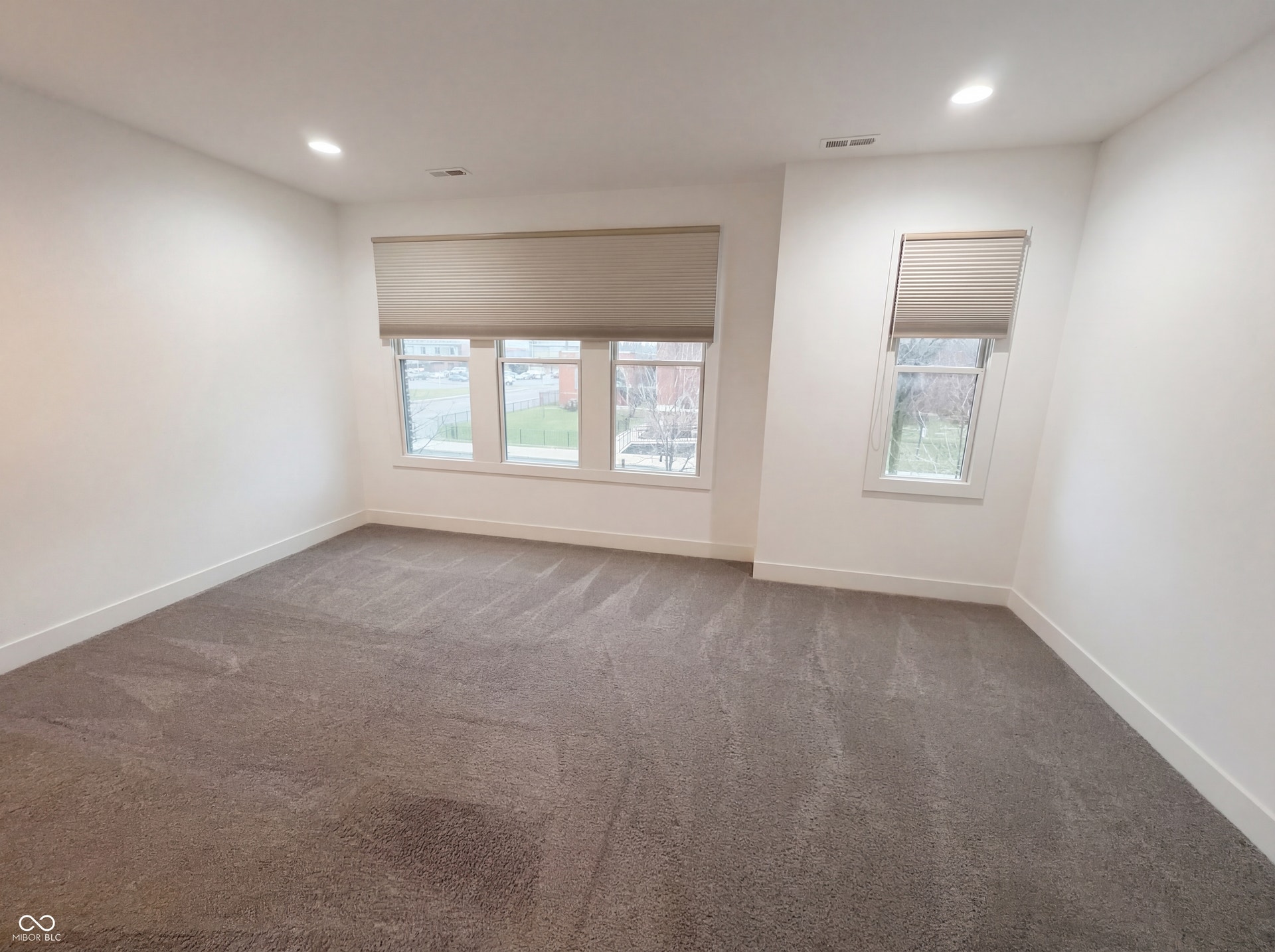 Spacious room featuring plush gray carpeting, crisp white walls, and multiple windows with included cellular shades