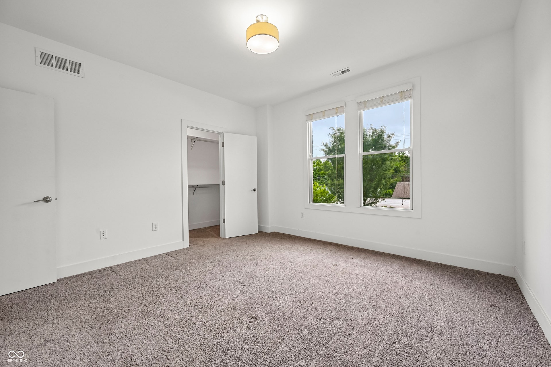 Bright room featuring a pair of windows, neutral carpet flooring, white walls, a built-in closet with shelving, and a flush mount ceiling light