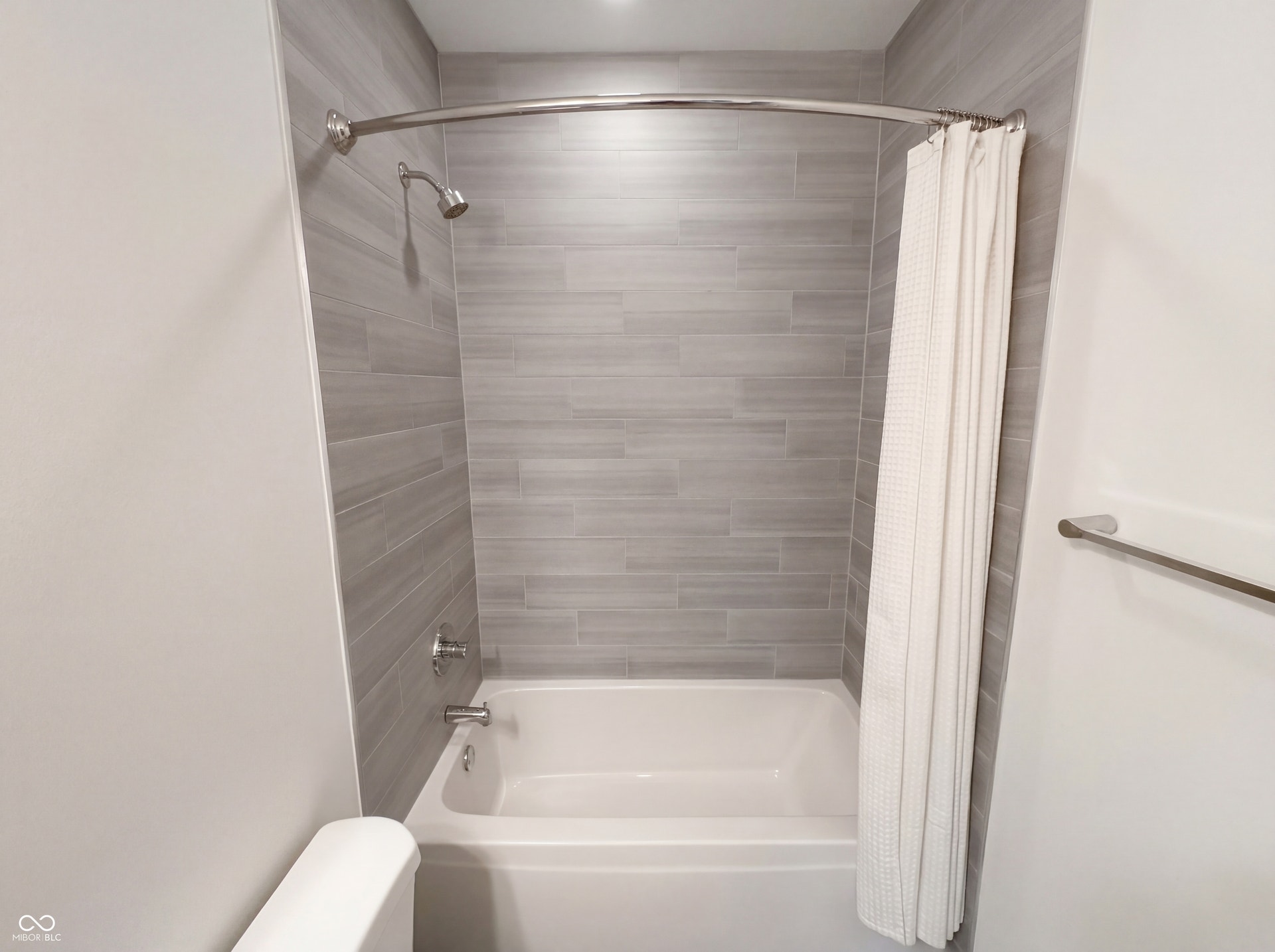 Bathtub-shower combination featuring light gray subway tile surround and brushed nickel fixtures