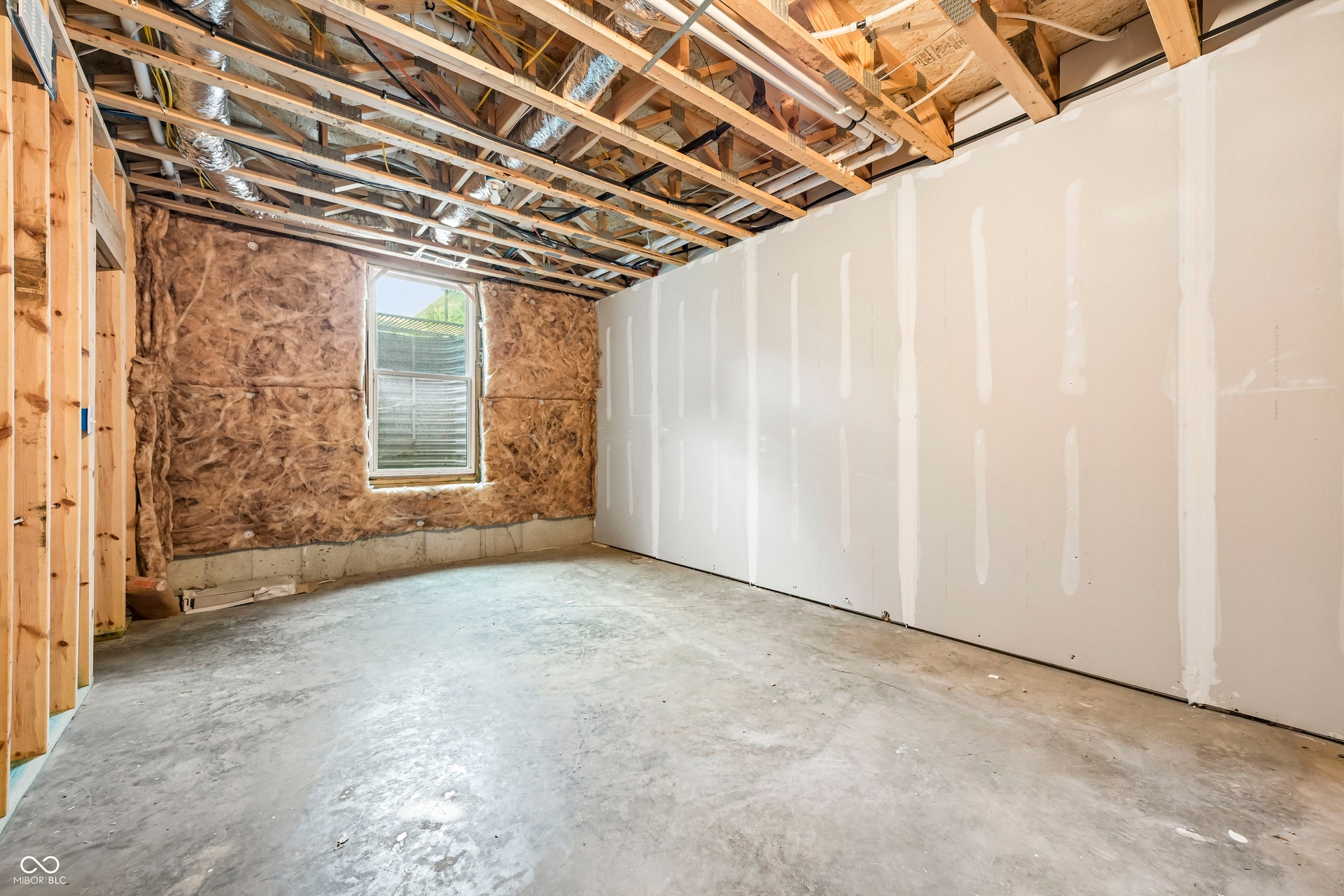 Unfinished basement space featuring exposed wooden ceiling joists, concrete flooring, and an egress window
