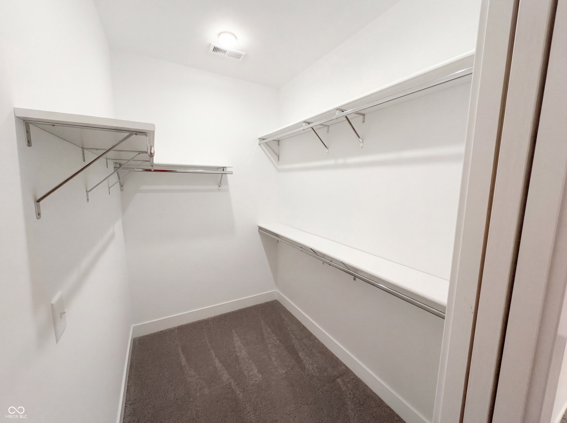 Walk-in closet featuring white walls, multi-level shelving, chrome hanging rods, recessed ceiling lighting, and carpet flooring