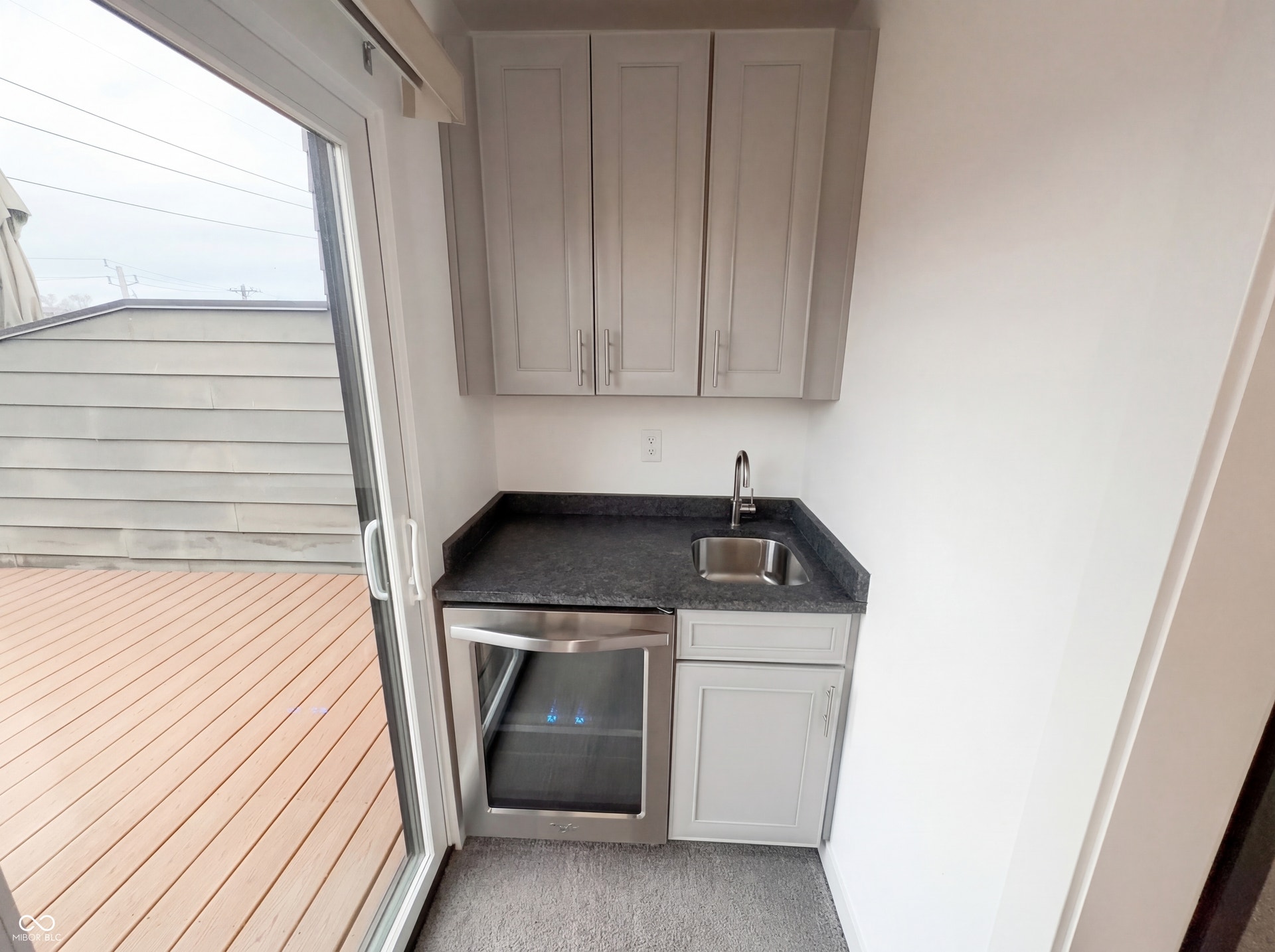 Compact wet bar featuring light gray shaker cabinetry, dark countertop, undermount stainless steel sink with gooseneck faucet, and an under-counter beverage refrigerator
