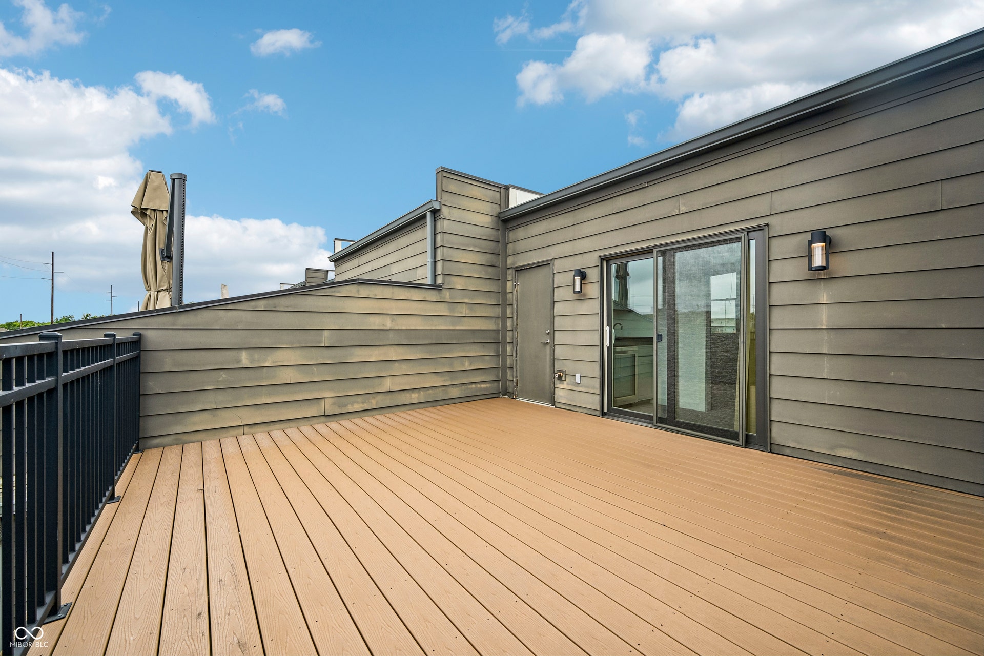 Rooftop deck featuring composite wood-finish flooring, dark metal railings, horizontal siding, and a sliding glass door entry