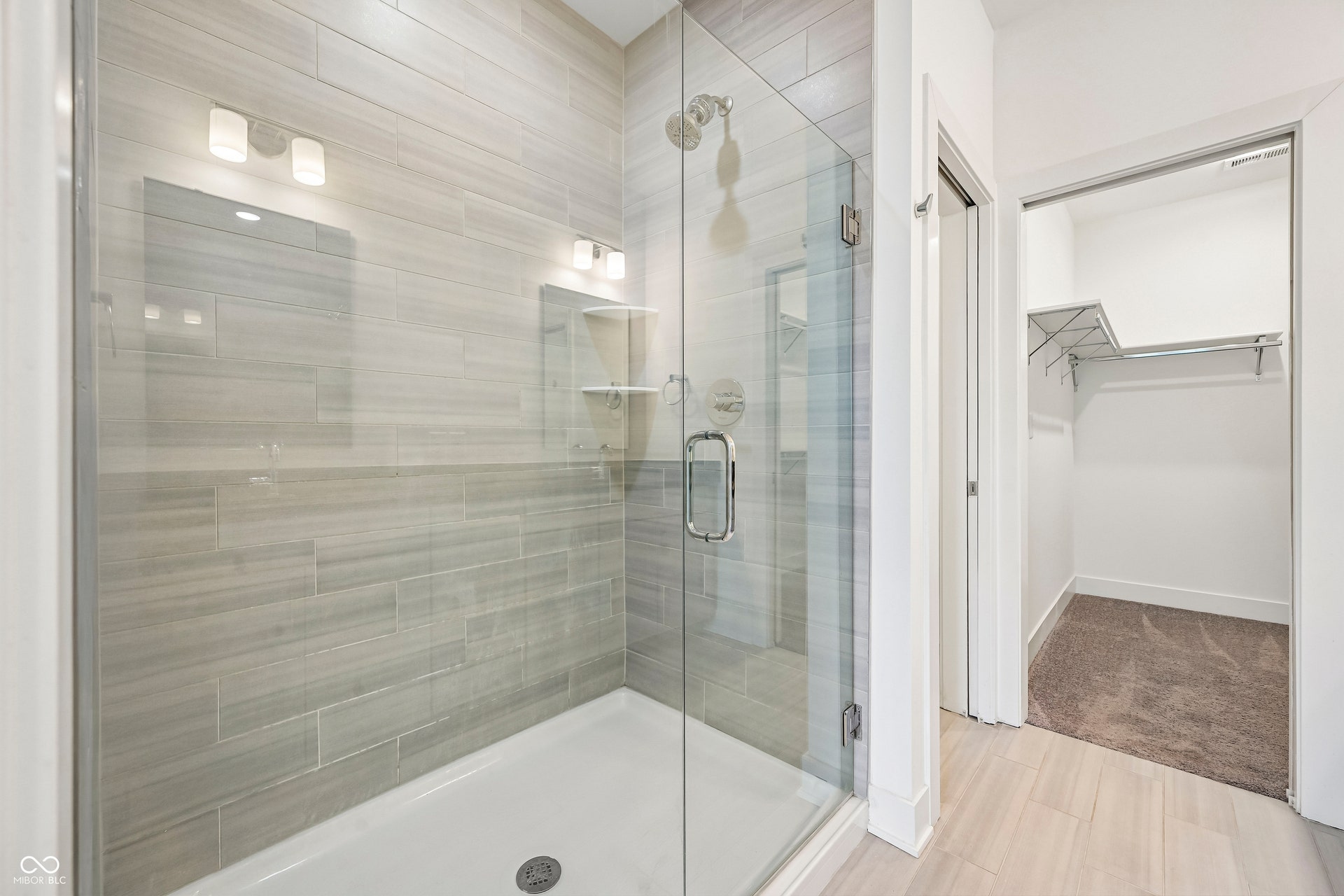 Glass-enclosed shower with horizontal tile surround and integrated shelving