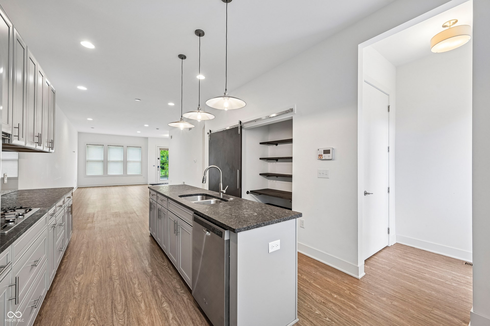 Kitchen featuring an island with integrated sink, stainless steel dishwasher, and pendant lighting