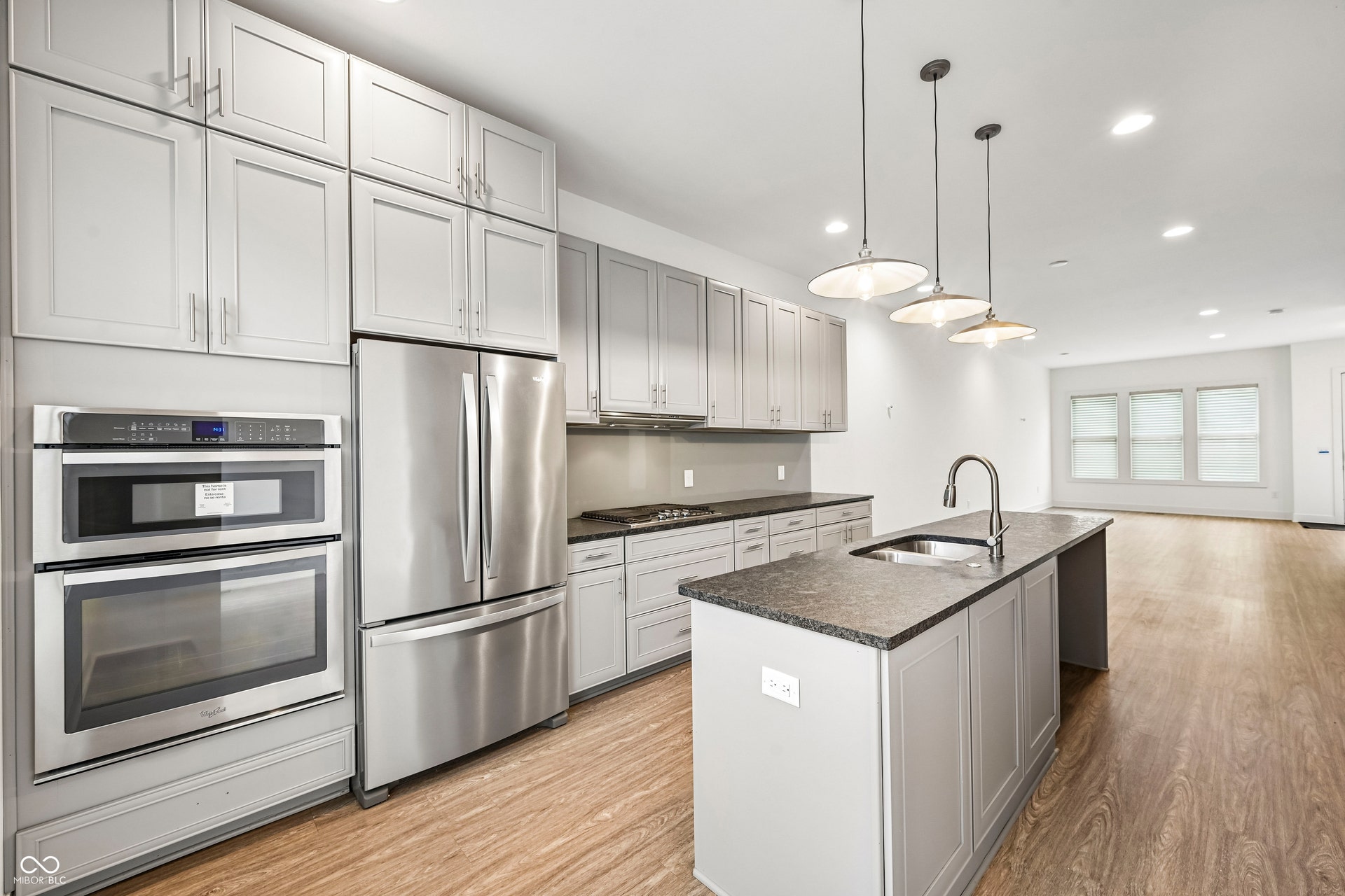 Kitchen featuring a large island with sink, stainless steel appliances, light gray cabinetry, dark countertops, and wood-finish flooring