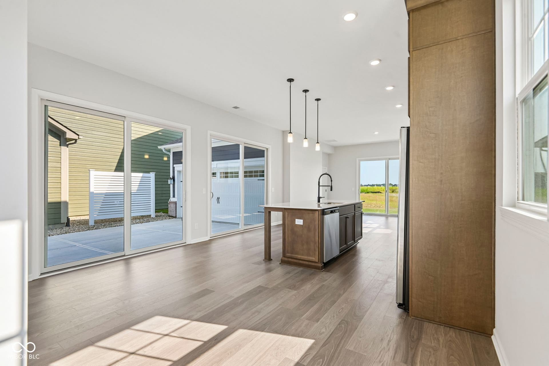 15691 Showdown Road, Noblesville, IN 46060 Open-concept interior featuring wood-finish flooring, a kitchen island with pendant lighting, stainless steel appliances, and multiple sliding glass doors